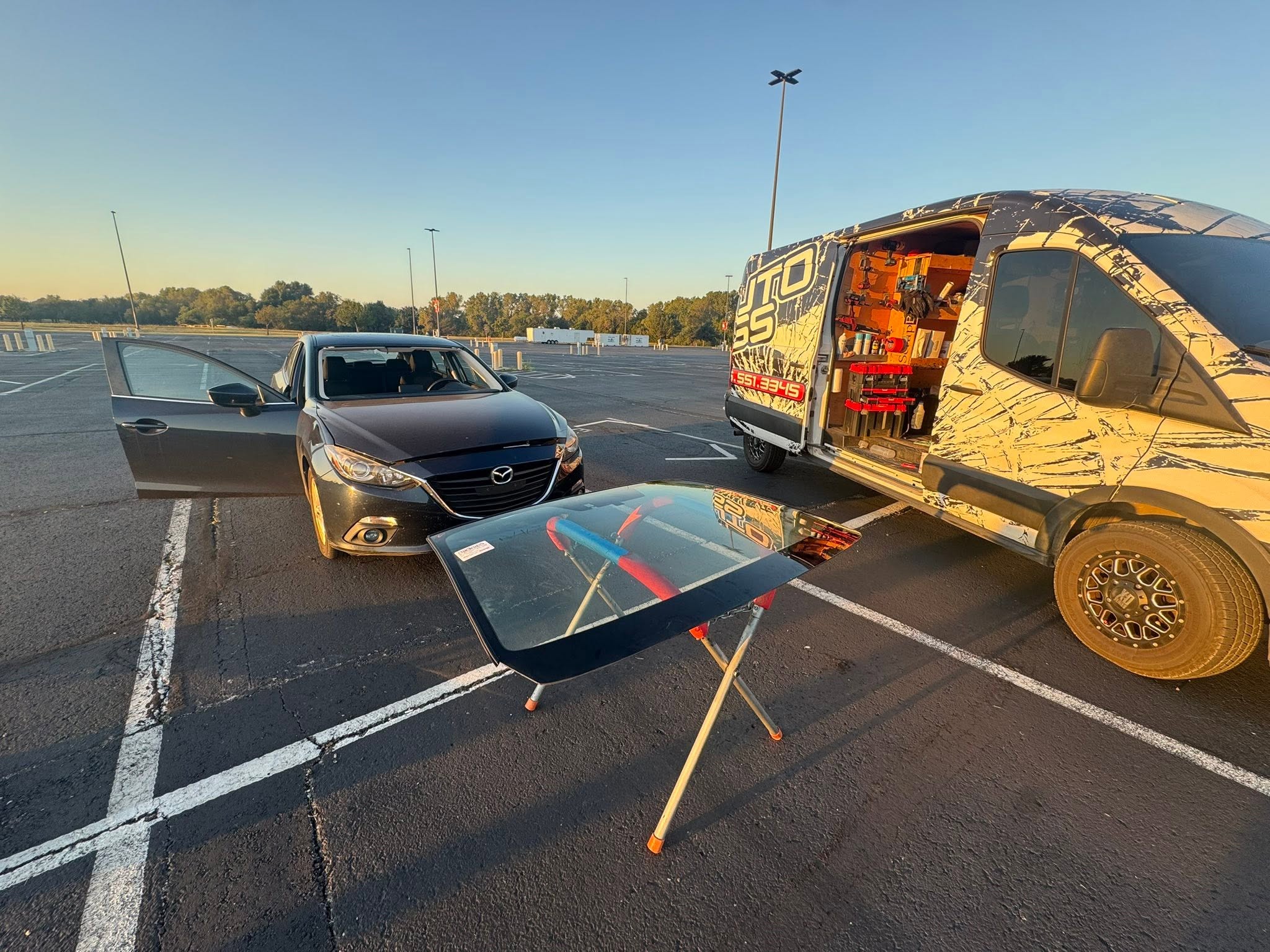 S&H mobile van parked in lot with windshield on installation stand at sunrise