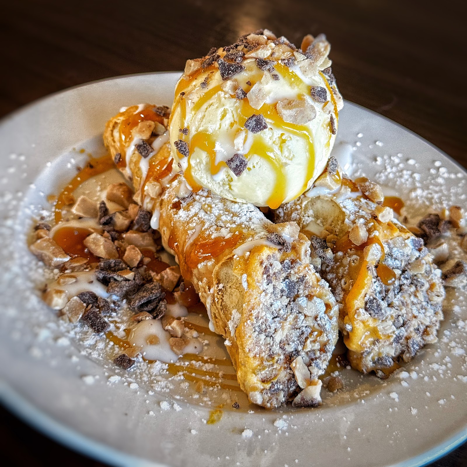Cannoli dessert topped with vanilla ice cream, caramel drizzle, and toffee crumbles