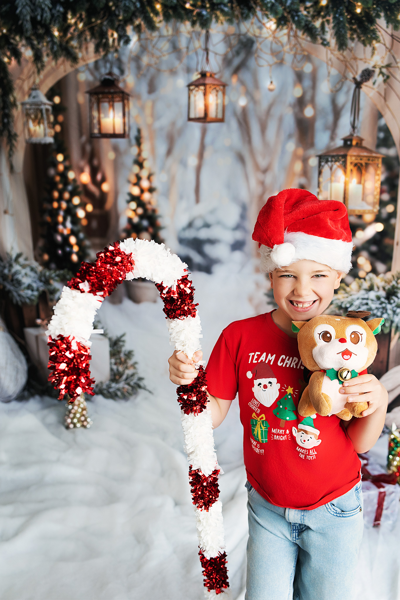 Smiling boy in Santa hat holding festive candy cane and plush reindeer