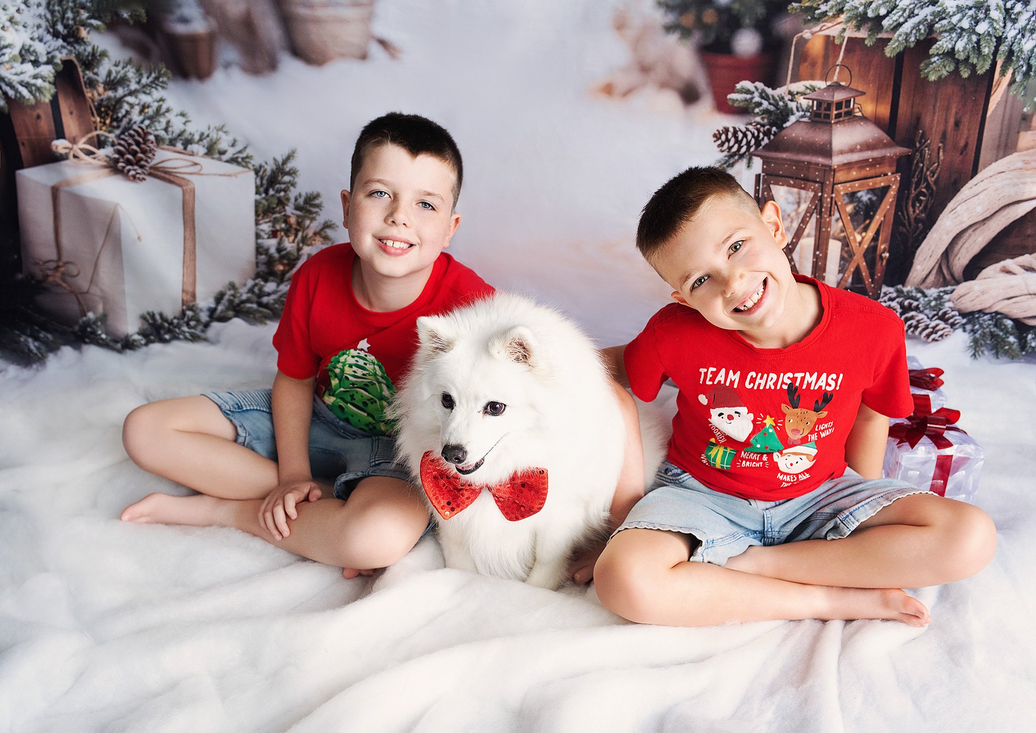 Two boys with their white dog in red bow tie on the snow