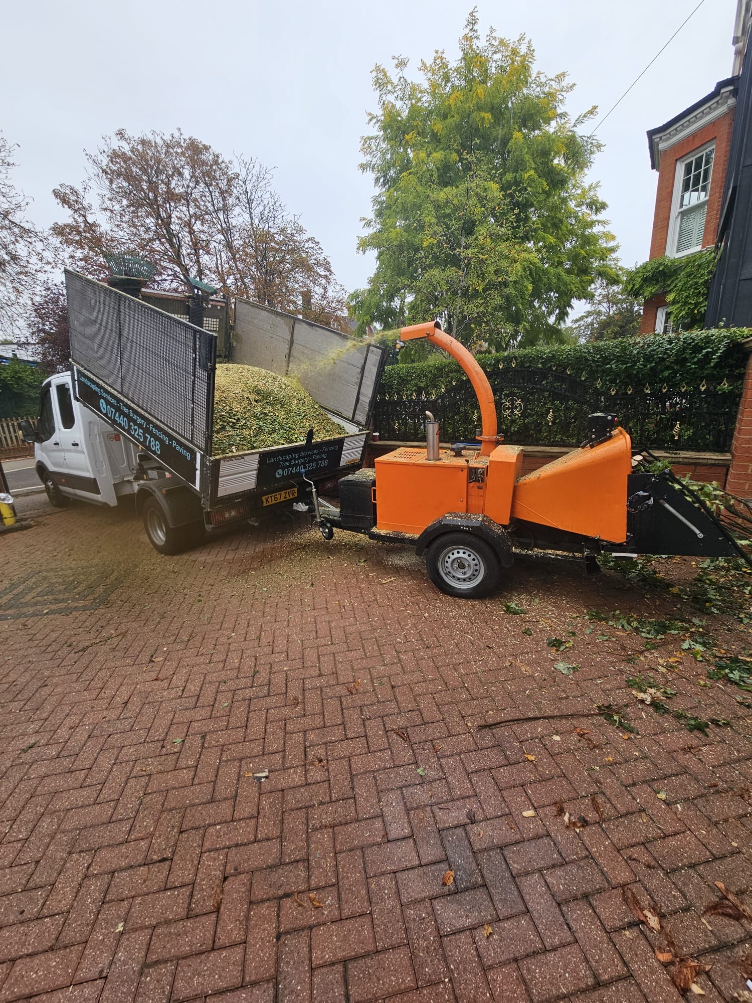 Toby's commercial wood chipper attached to his work van, processing green garden waste on a residential driveway in Wembley.