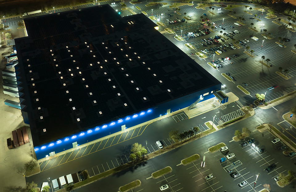 High-angle night view of high-output LED yard, perimeter fence line, building exterior wall packs, and parking lighting at a mission-critical distribution facility