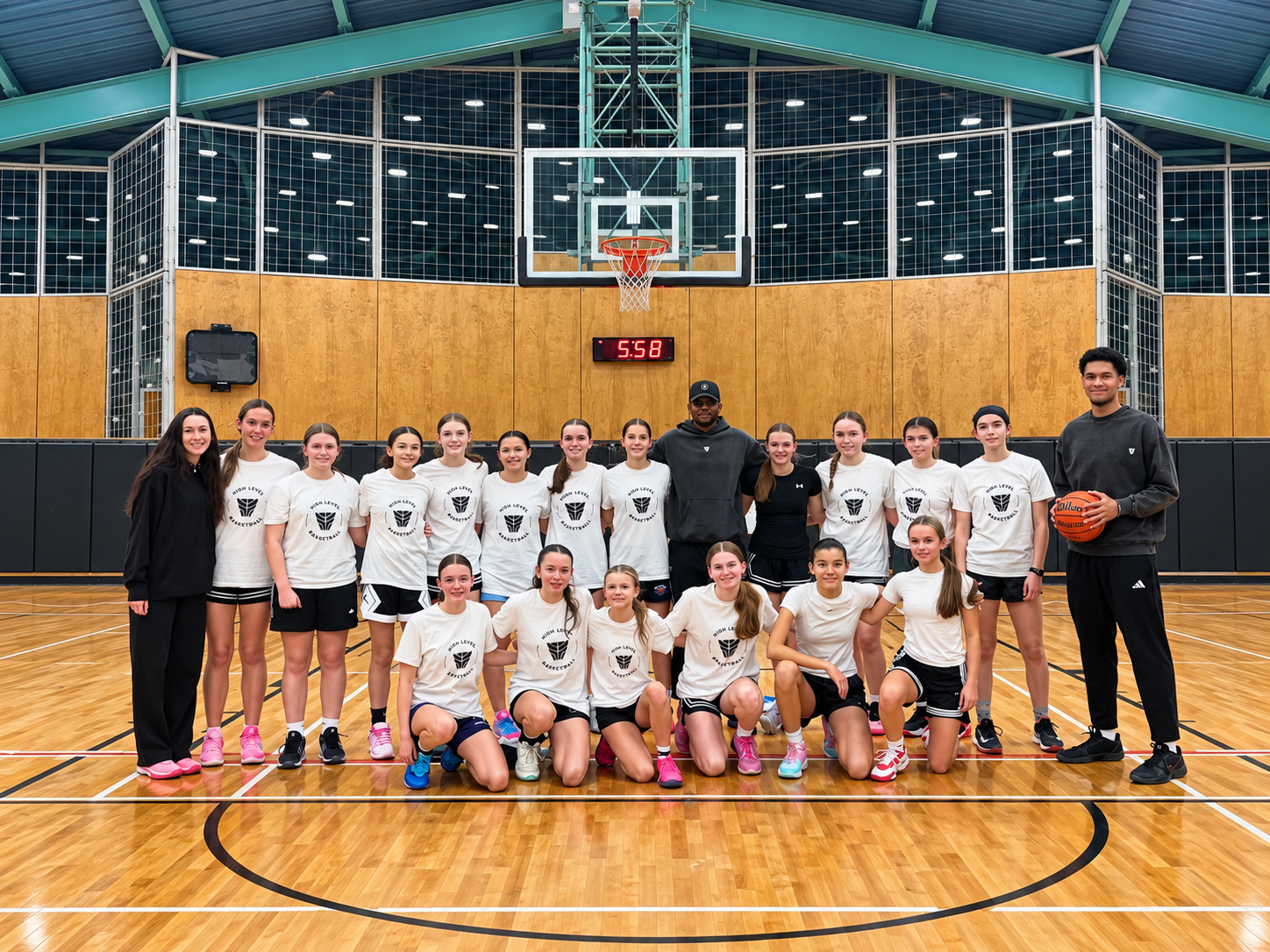High Level Basketball girls team and coaches smiling together on court after practice