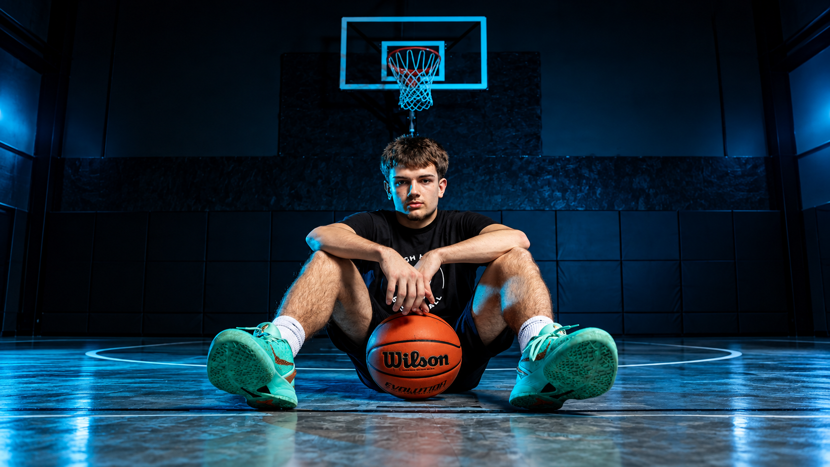 Young basketball player seated on court with basketball under the hoop, ready for 1-on-1 private training