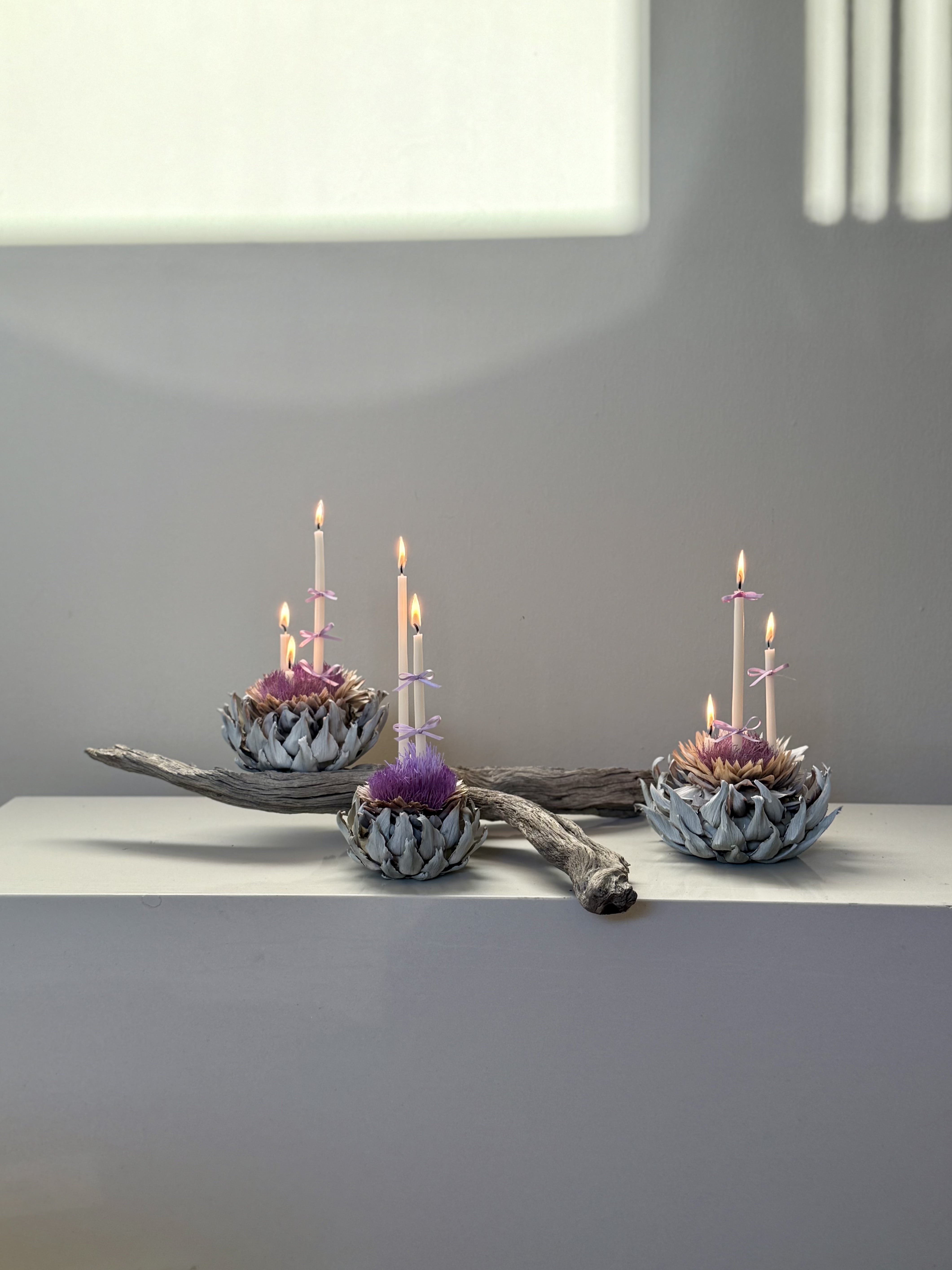 Sculptural candle composition of pale dried artichokes holding taper candles tied with lilac ribbons by Soulform Florals, Los Angeles