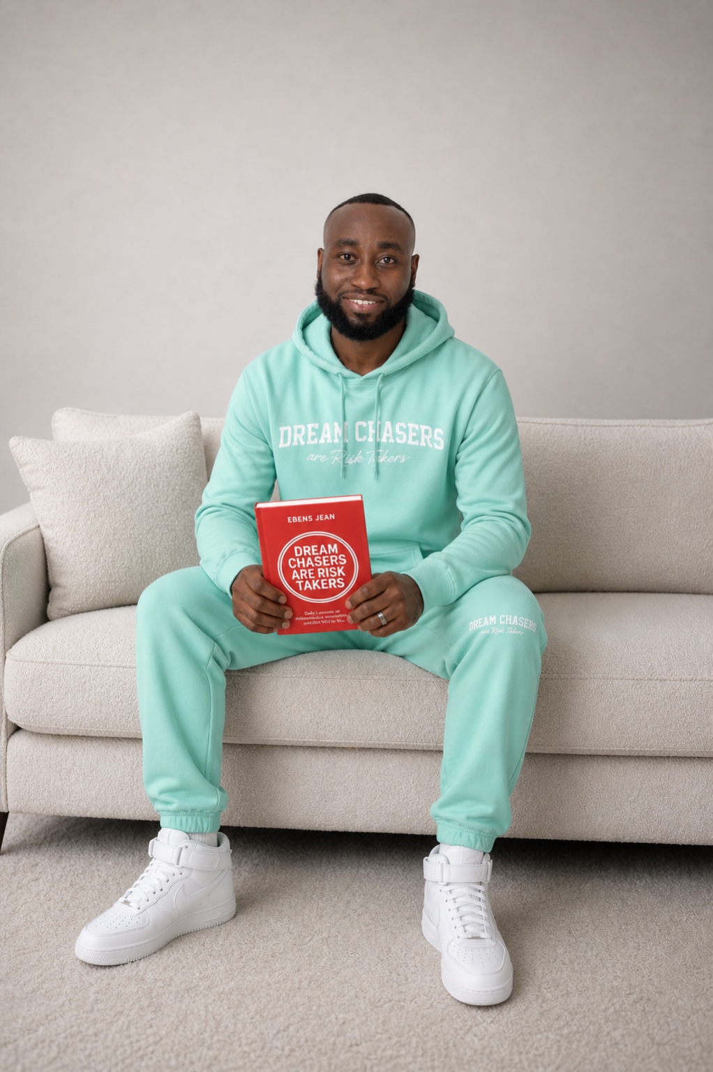 Ebens Jean on sofa in mint green Dream Chasers hoodie holding red copy of the book