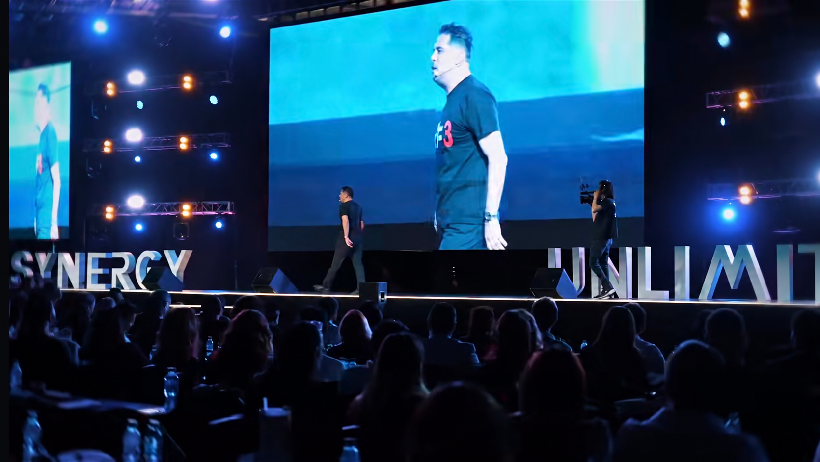 Jorge Serratos speaking on stage at Synergy Unlimited in front of a live audience