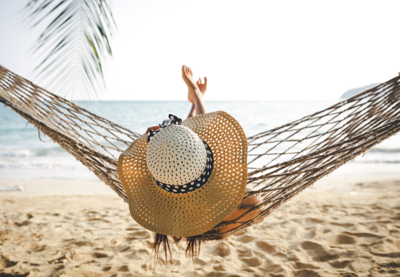 Relaxing in a woven hammock between palm trees on a tropical beach overlooking the turquoise ocean
