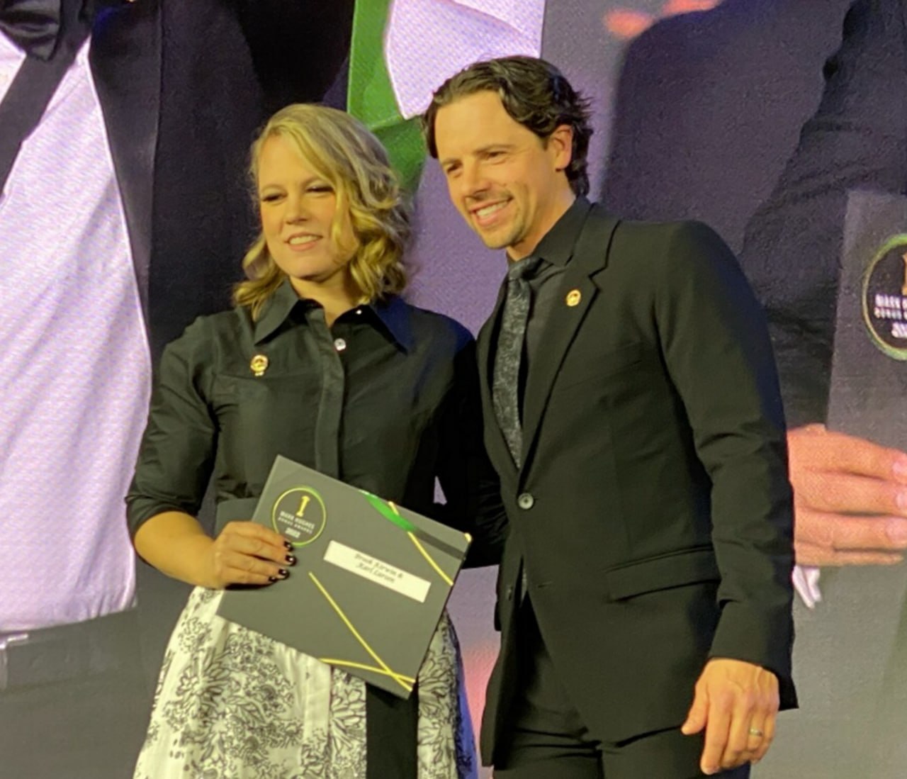 Karl and Brook receiving an achievement award on stage.