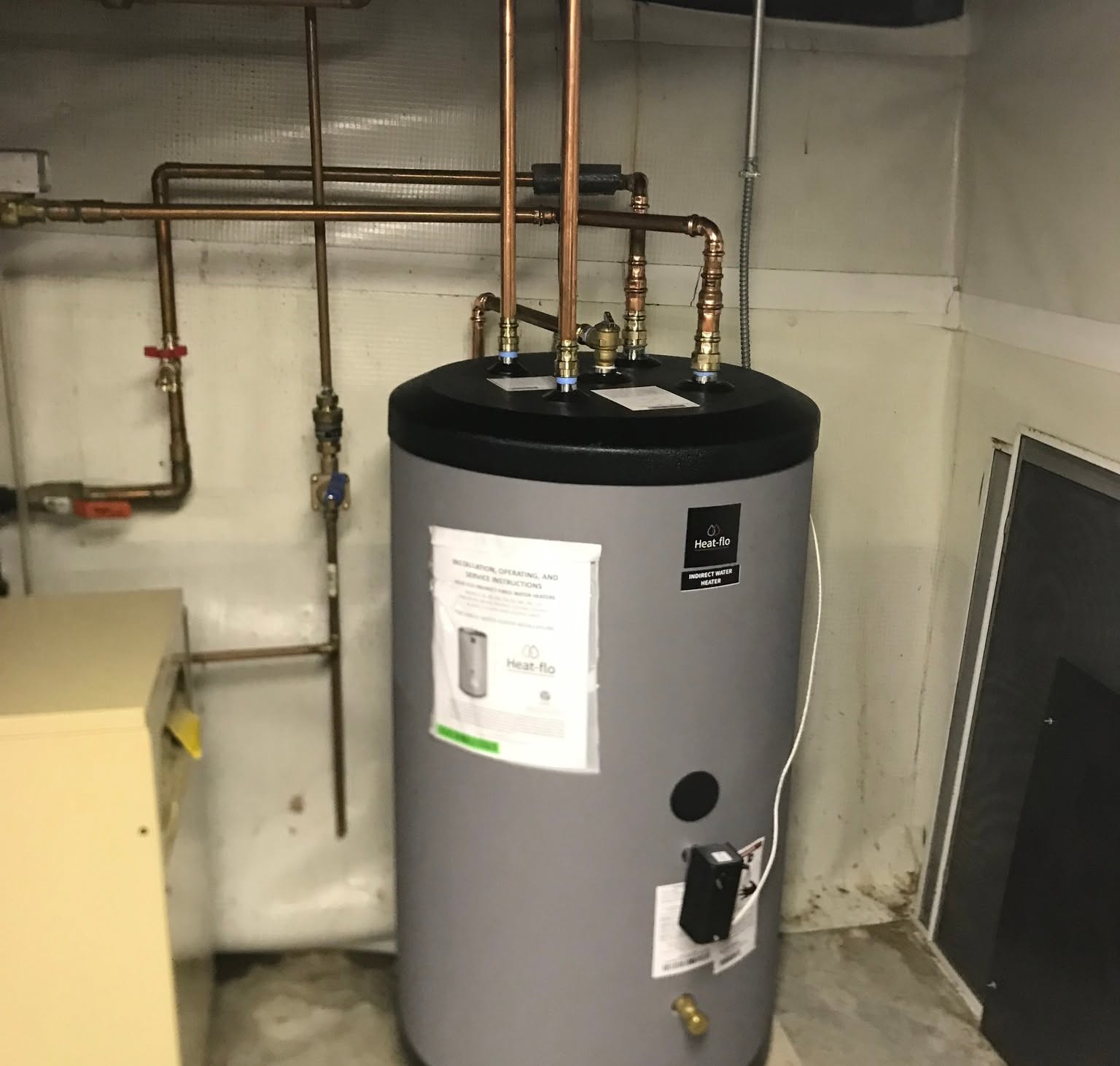 Heat-Flo high-efficiency indirect-fired water heater tank piped in rigid copper with ProPress fittings, integrated aquastat controller, isolation ball valves, and boiler hydronic loop in a clean residential basement
