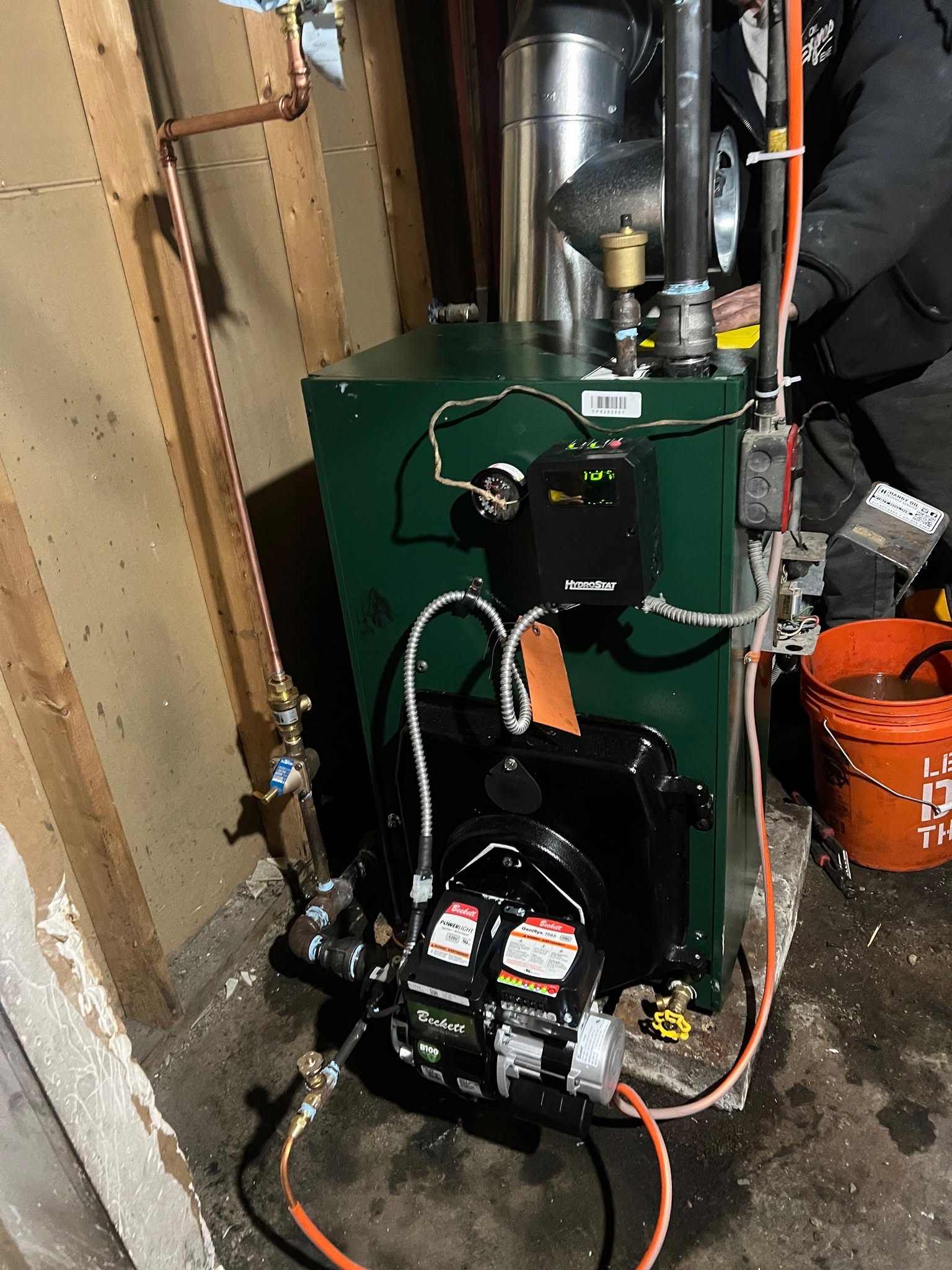 Forest green cast-iron residential oil boiler installation with digital HydroStat 3250-Plus controller displaying operating temperature, Beckett GeniSys burner, copper hydronic return, and galvanized smoke flue