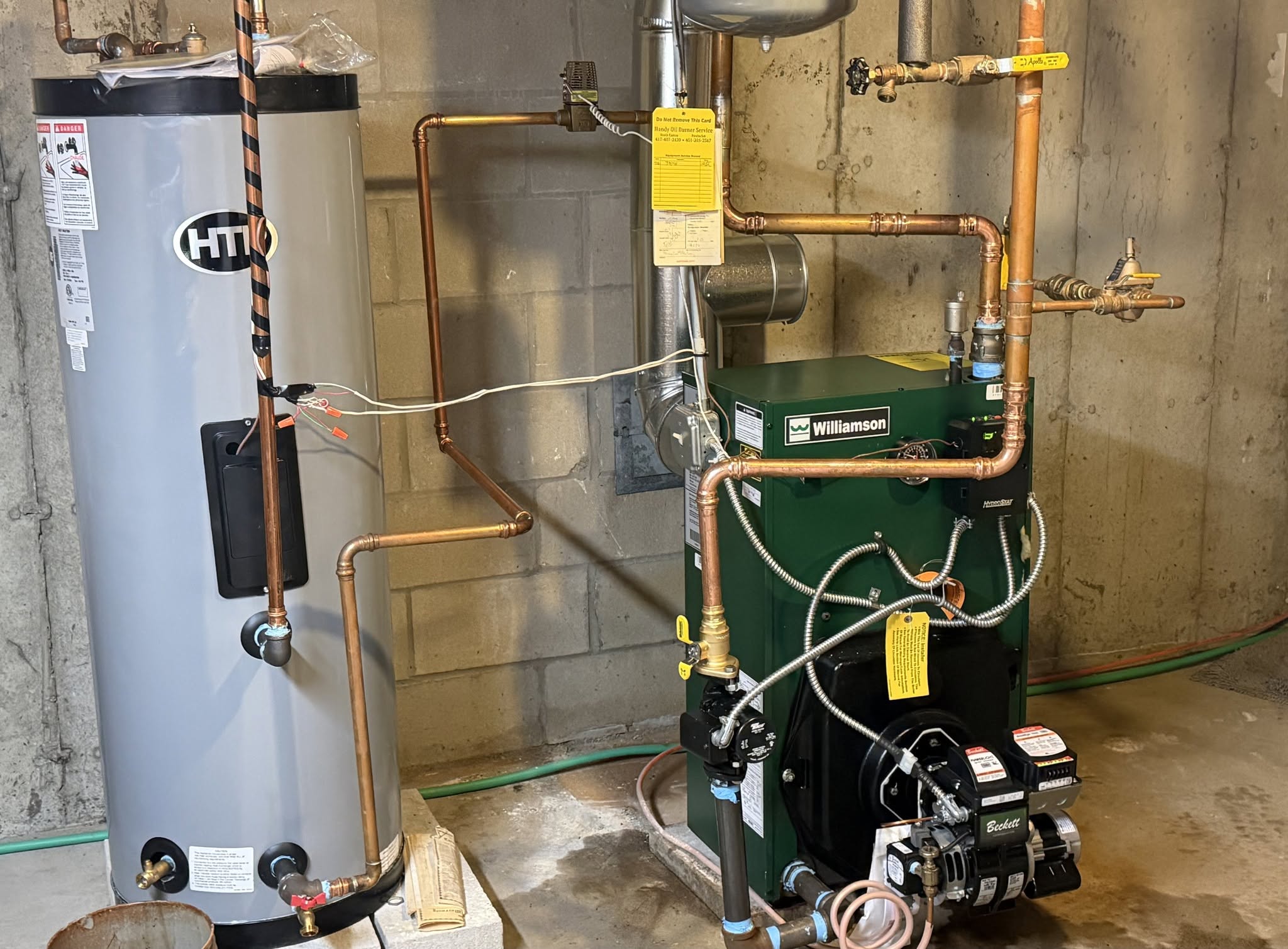 New green Williamson residential oil-fired cast-iron boiler equipped with Beckett flame retention oil burner, Hydrolevel Hydrostat temperature limit control, Taco circulator pump, and companion HTP indirect domestic hot water storage tank in a Massachusetts home