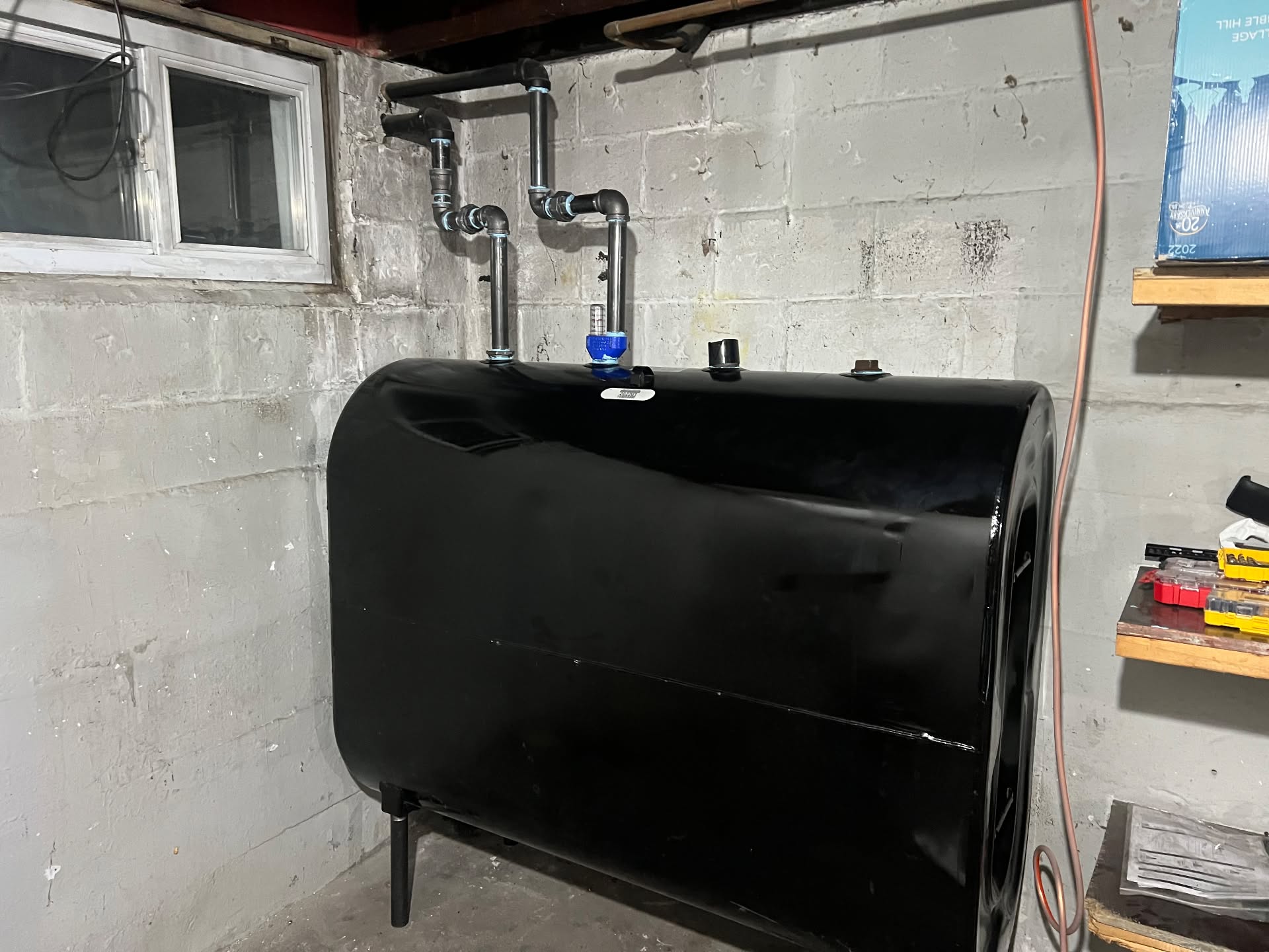 Black finish Granby residential heating oil storage tank installed in a concrete foundation basement with black-iron top vent and fill piping, visual float level gauge, and solid floor clearance