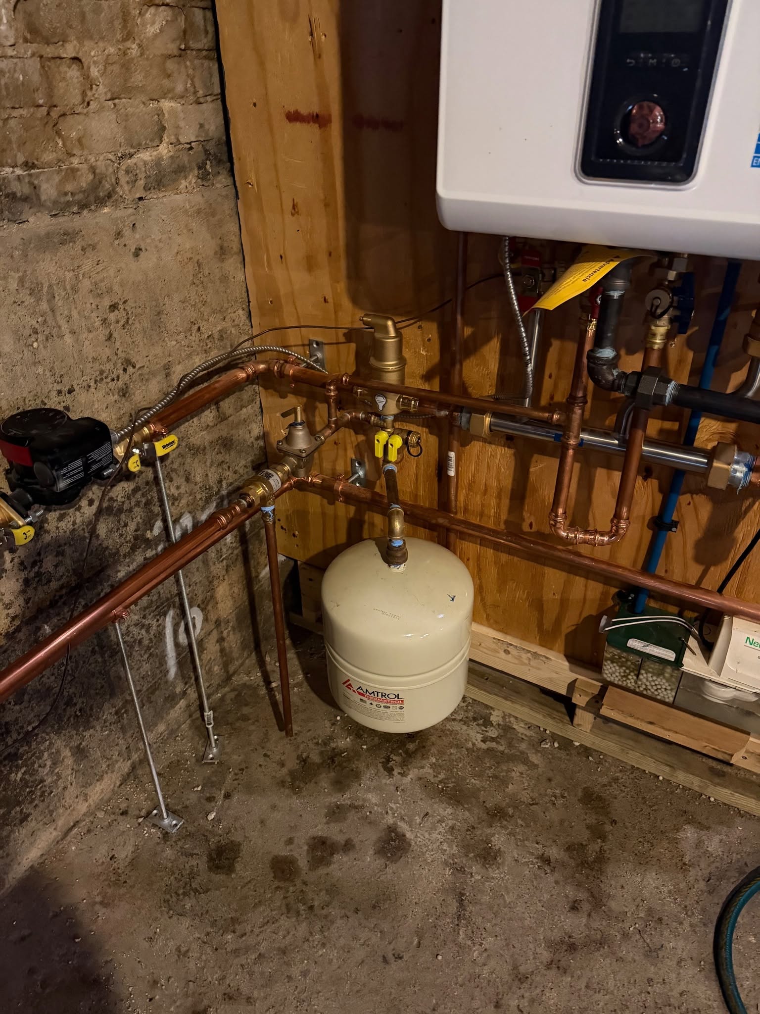 Amtrol Therm-X-Trol hydronic expansion tank mounted beneath wall-hung condensing boiler, showing copper press piping manifold, Spirovent air eliminator, pressure reducing fill valve, and acid condensate neutralizer