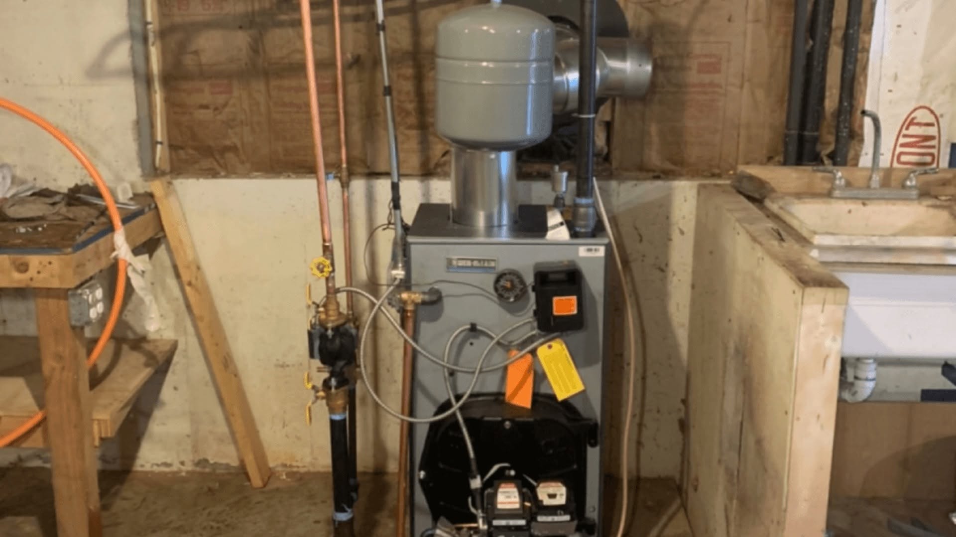 Weil-McLain gray cast-iron oil boiler with Beckett GeniSys burner, overhead gray hydronic diaphragm expansion tank, Taco circulator pump, pressure-temperature gauge, and official service inspection tags