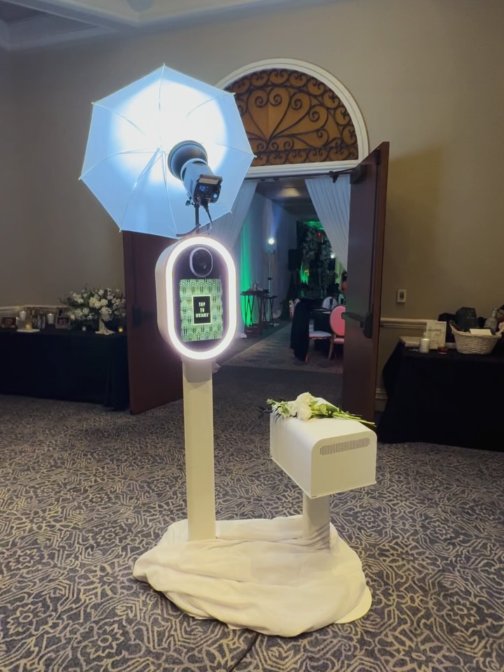Grand ballroom entrance photo booth with fresh white florals, studio umbrella light, and Art Deco start screen