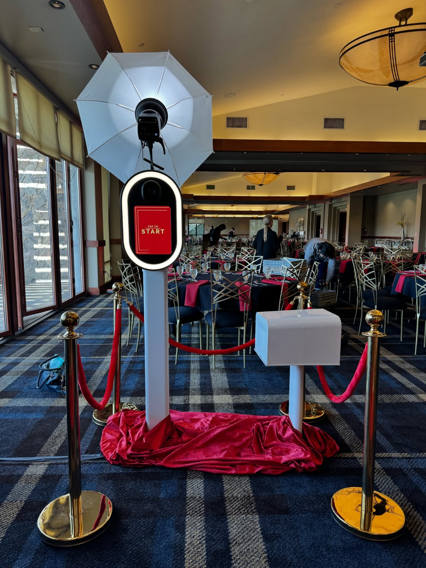 PRC white photo booth stationed in an elegant banquet hall with red velvet skirt and gold stanchions