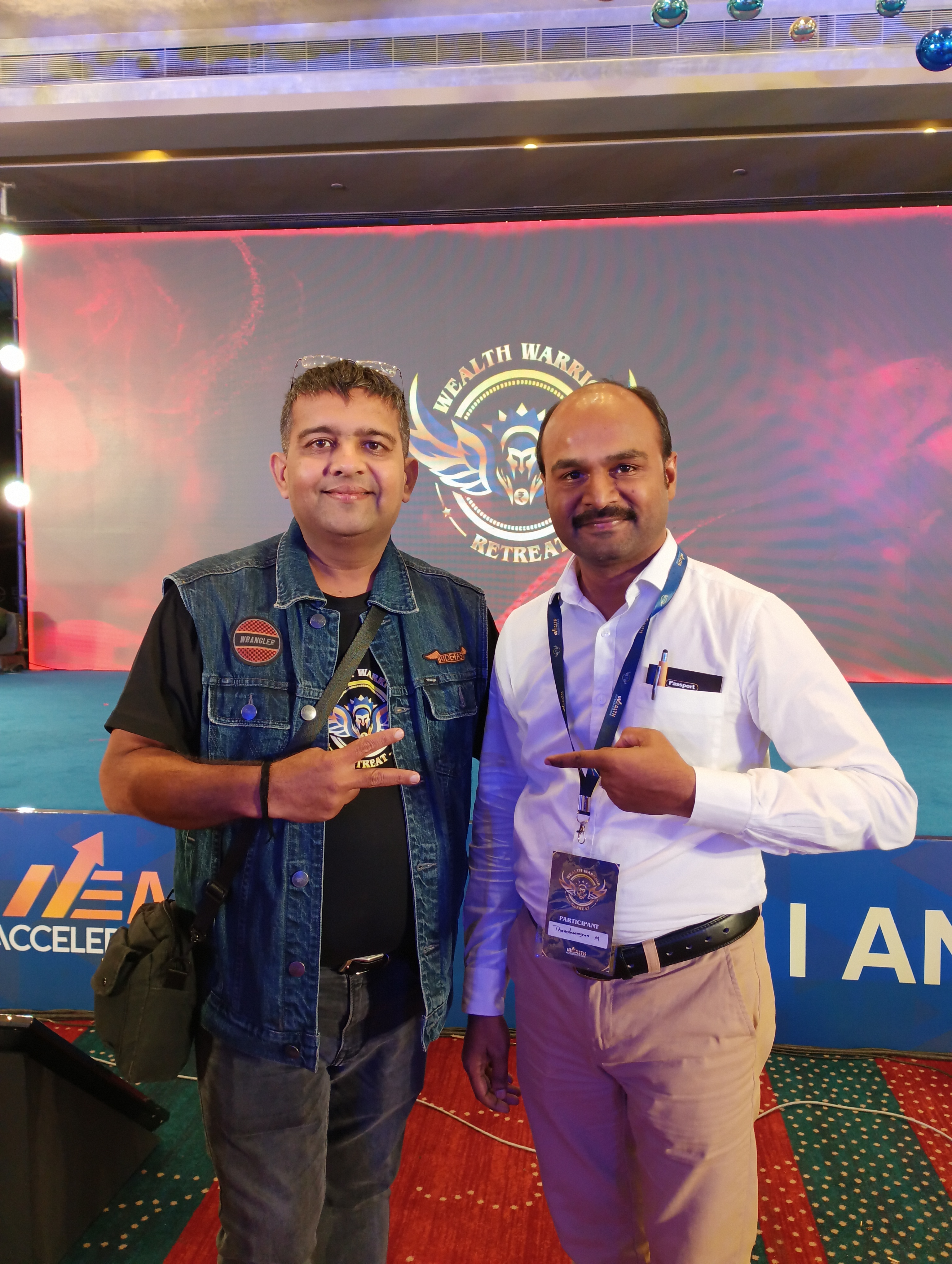 Thandavarayan M. with fellow coach in front of the Wealth Warrior Retreat stage backdrop in January 2025