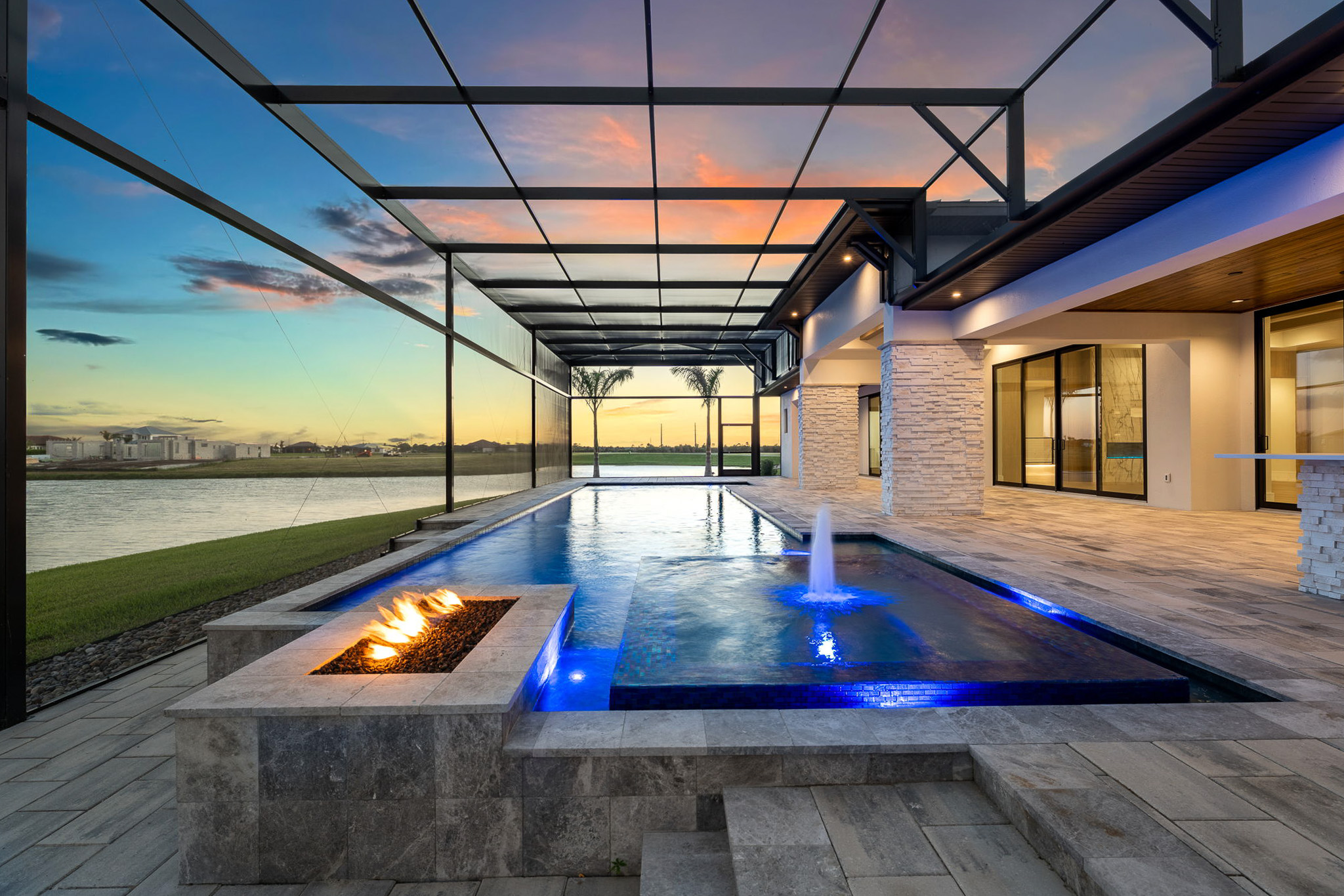 Screened luxury pool with illuminated fire pit and sunset lake view