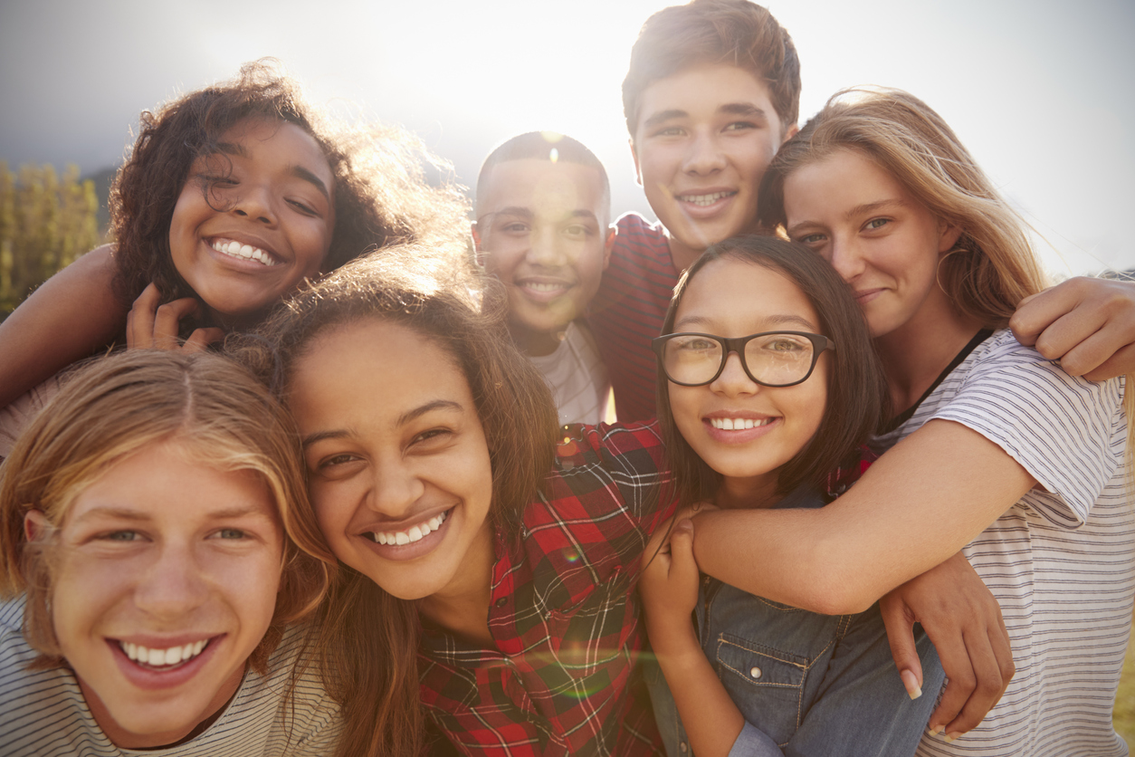 A diverse group of smiling teens together outdoors