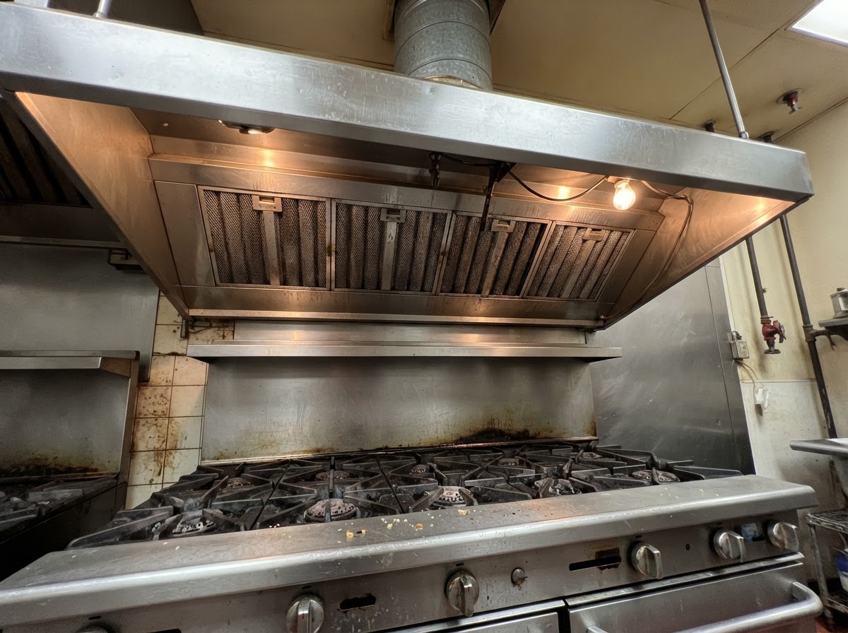 Commercial range hood directly above a gas range with burners