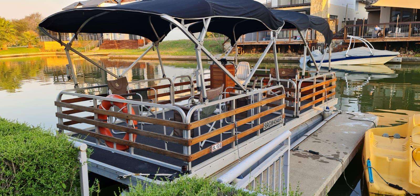 Main pontoon boat docked in tranquil estate canal water at golden hour with double canopy and wood railings