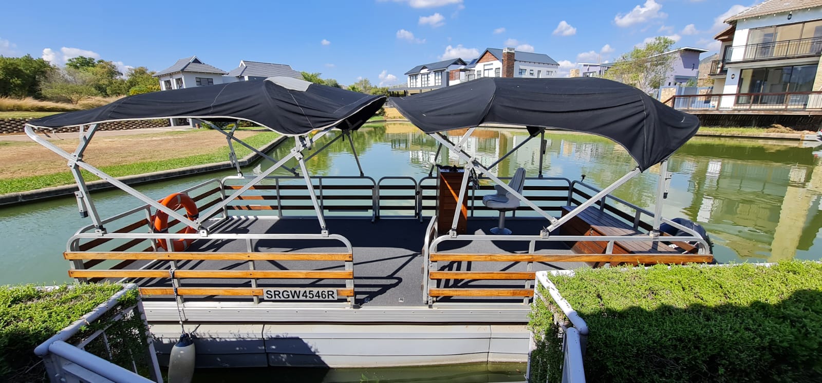 Main pontoon boat moored at the canal jetty, wide side and deck view under blue skies