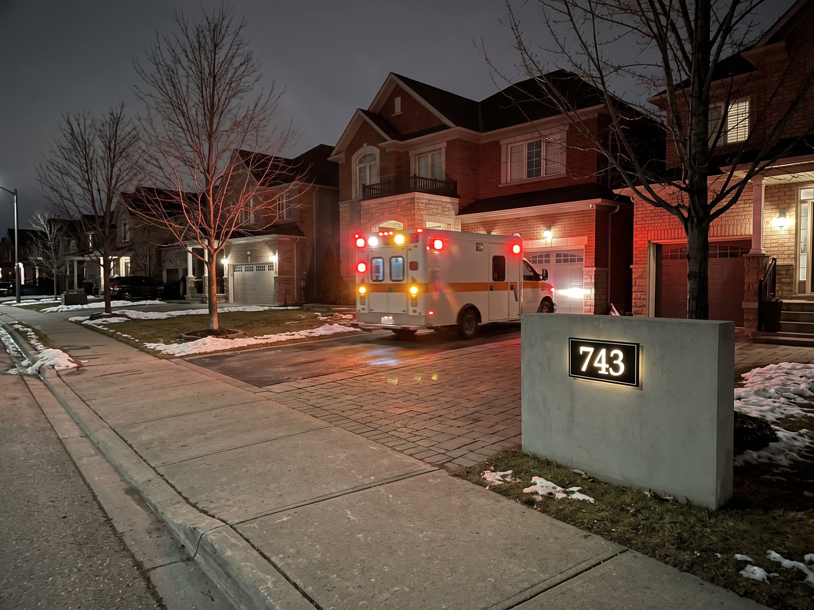 Ambulance on dark residential street with lit address wall at curb