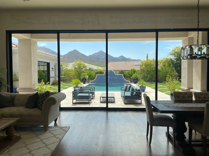 View through sliding glass doors to a completed backyard pool, patio furniture, turf diamond pavers, and mountain backdrop