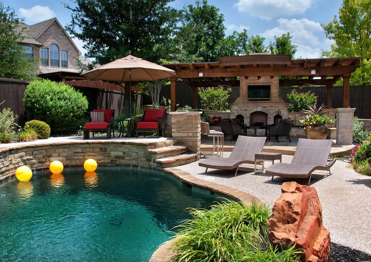 Completed backyard transformation featuring a pool, stone fireplace and TV under a wooden pergola, patio seating, and loungers