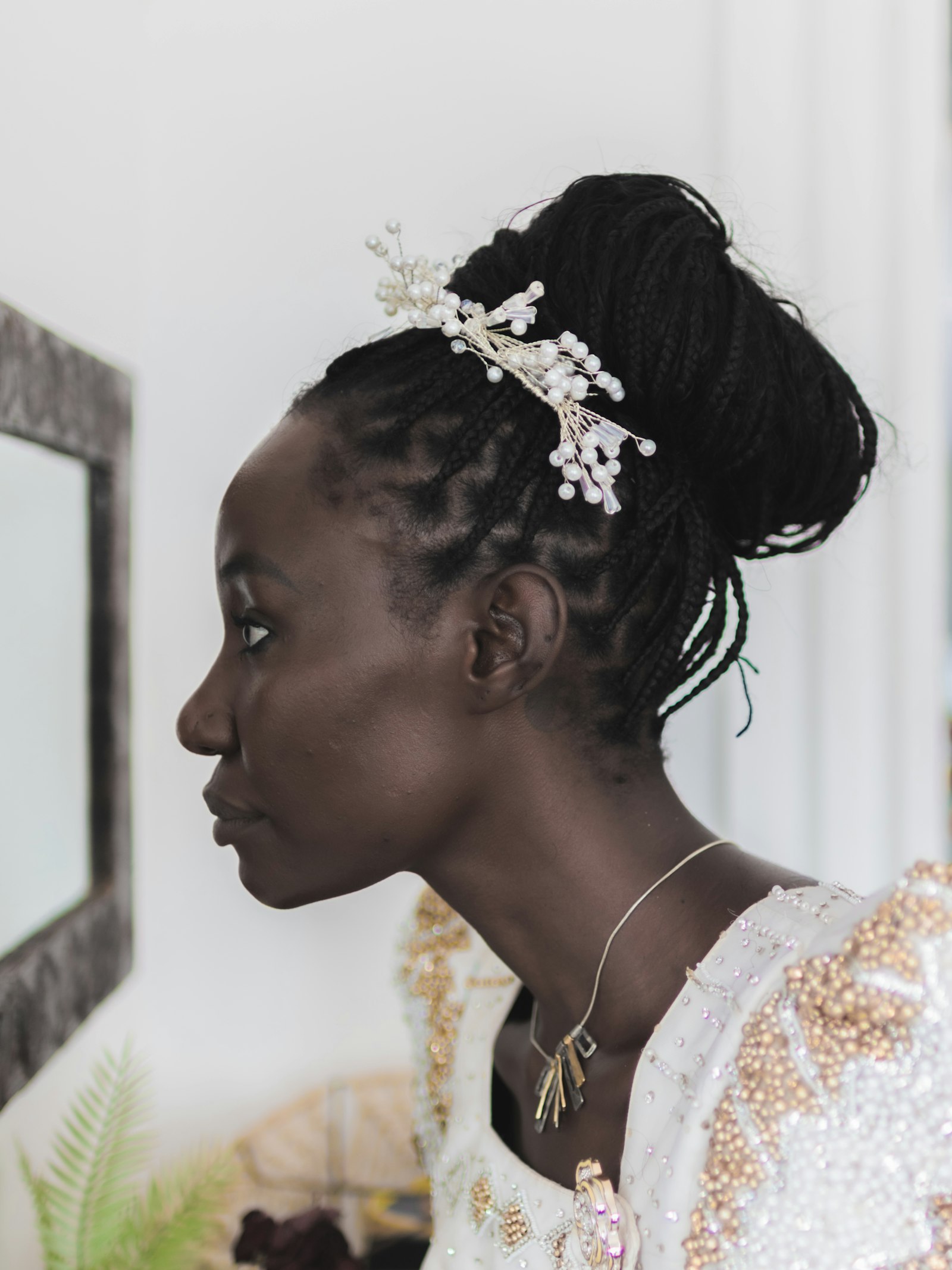 A radiant African bride wearing an elegant braided bun with a pearl hairpiece, showcasing bridal and formal occasion styling at La Salon in Pickering