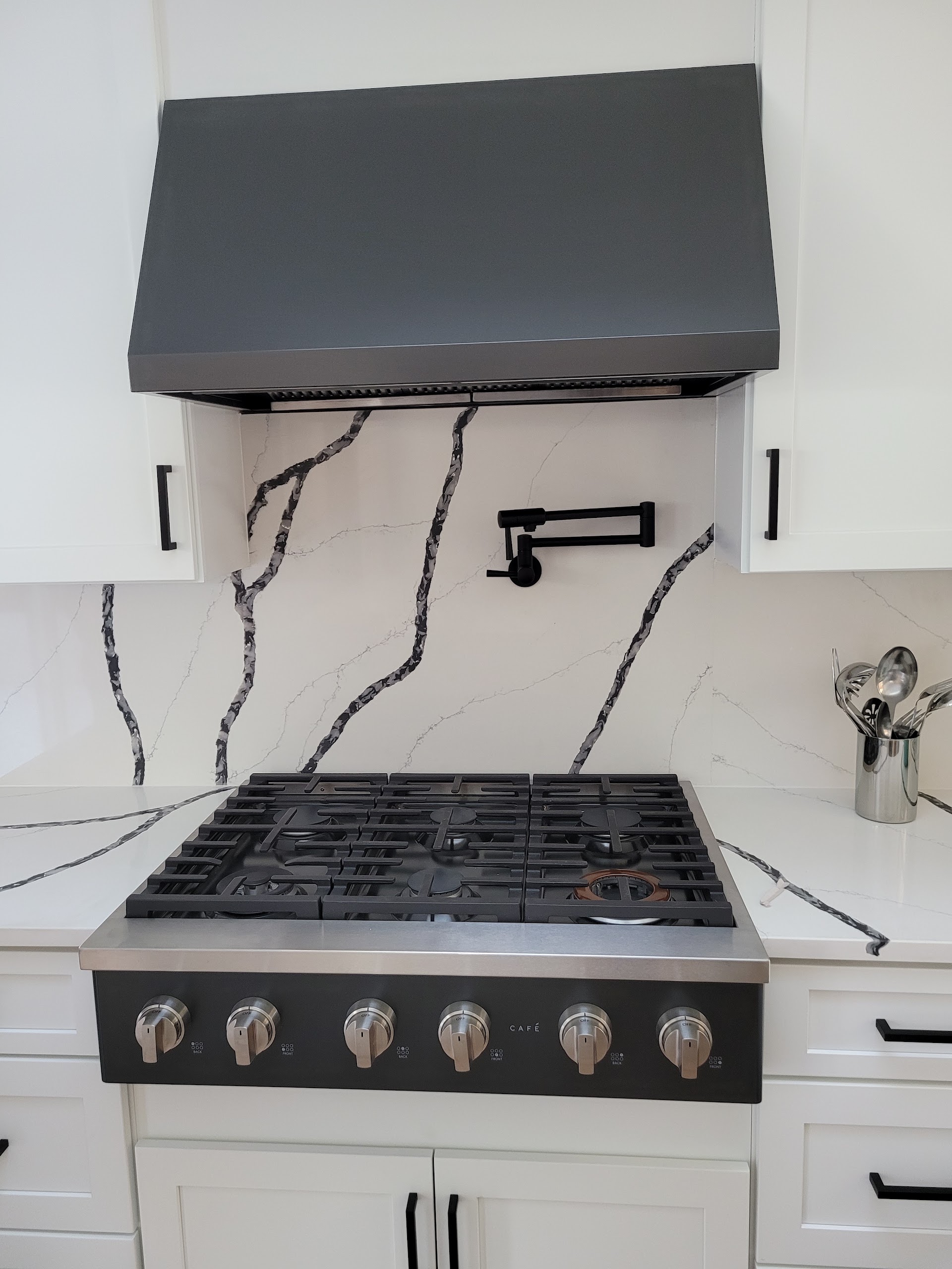Café gas cooktop with matching range hood and custom backsplash