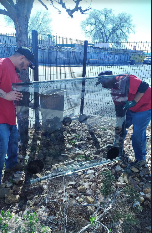 Two Glass on Wheels team members in red shirts safely handling a large clear glass panel with suction cups
