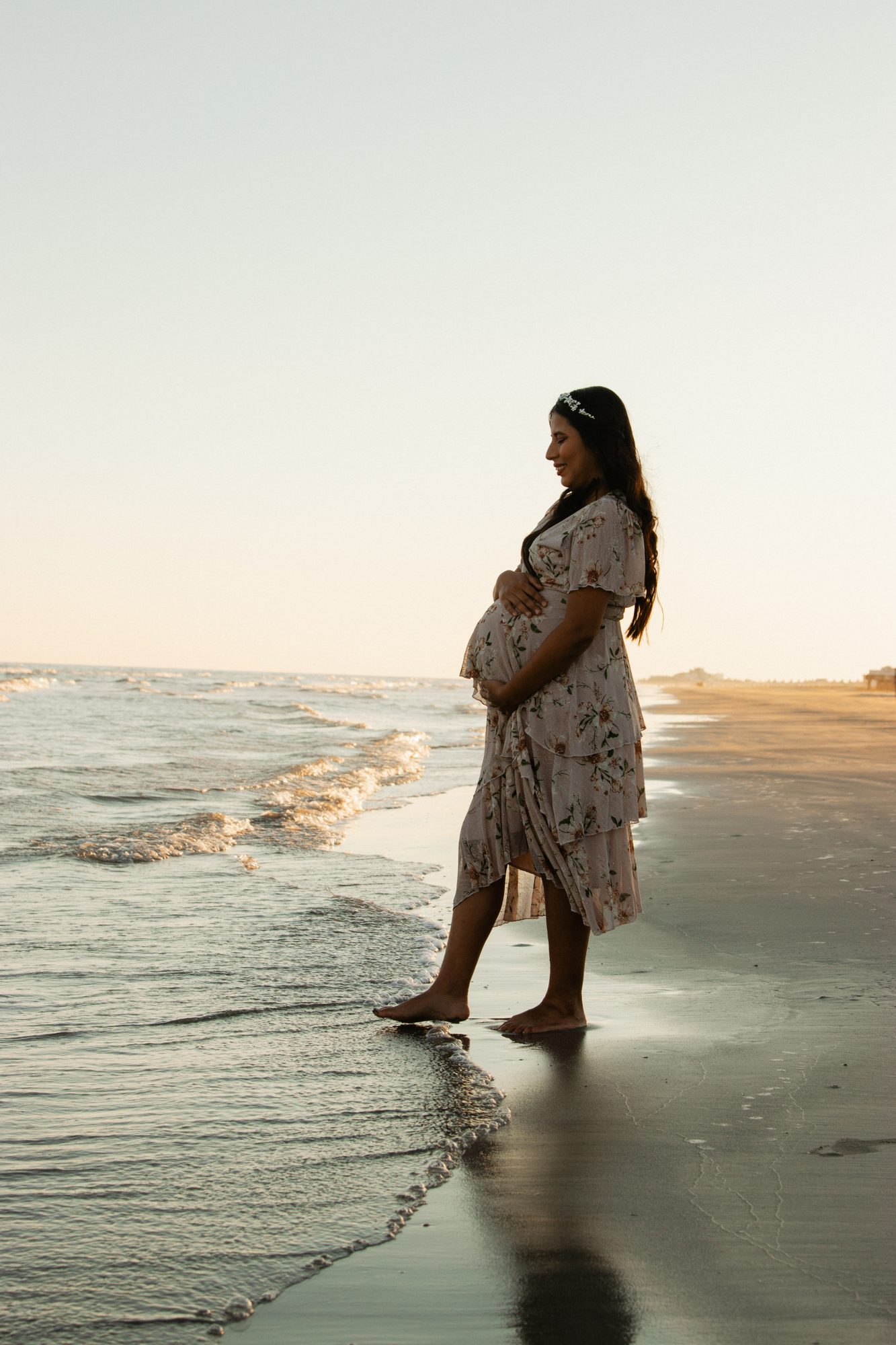 Expecting mom in profile at the water's edge at sunset