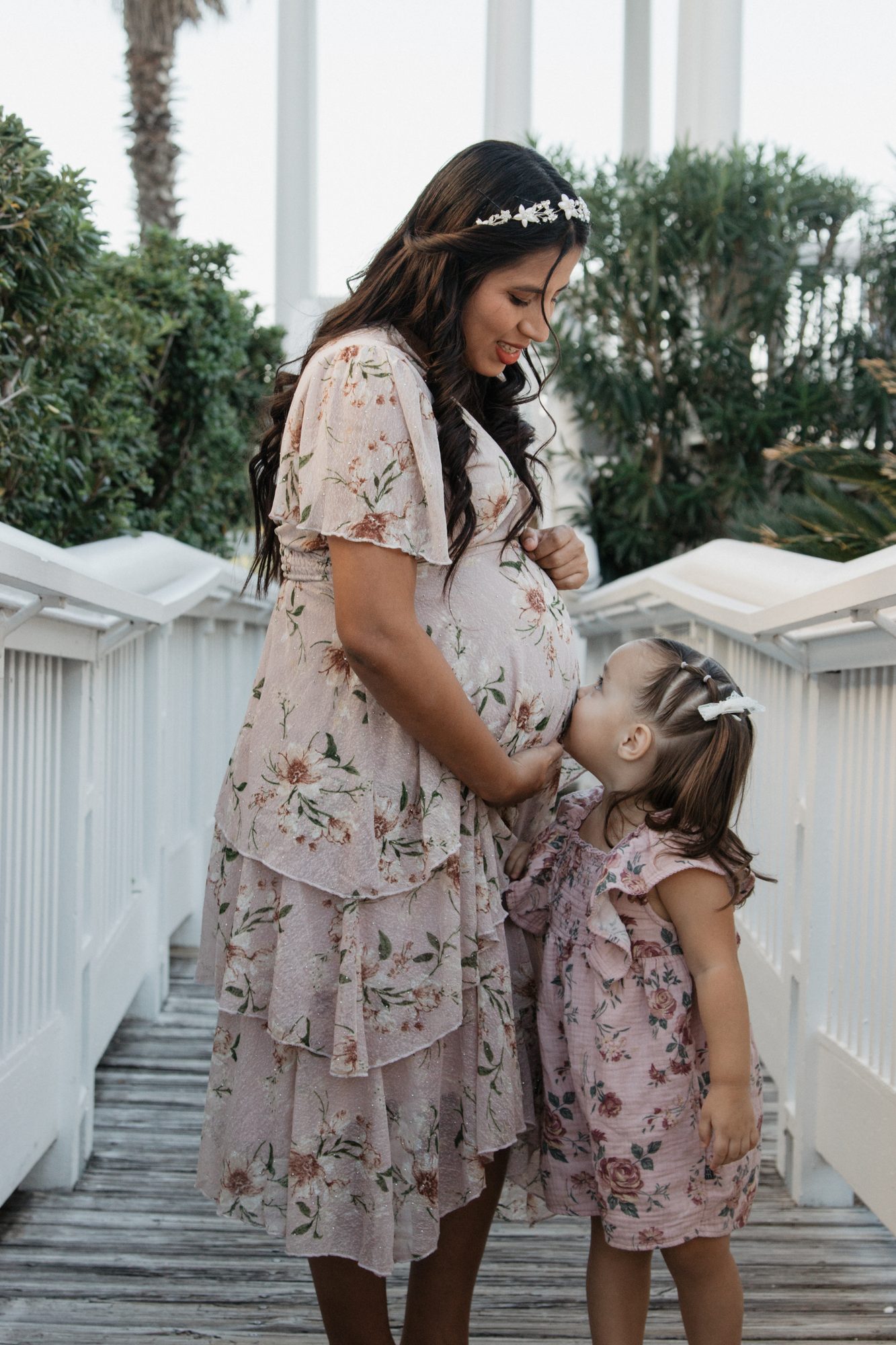 Mom and her little girl kissing her baby bump on a Galveston boardwalk