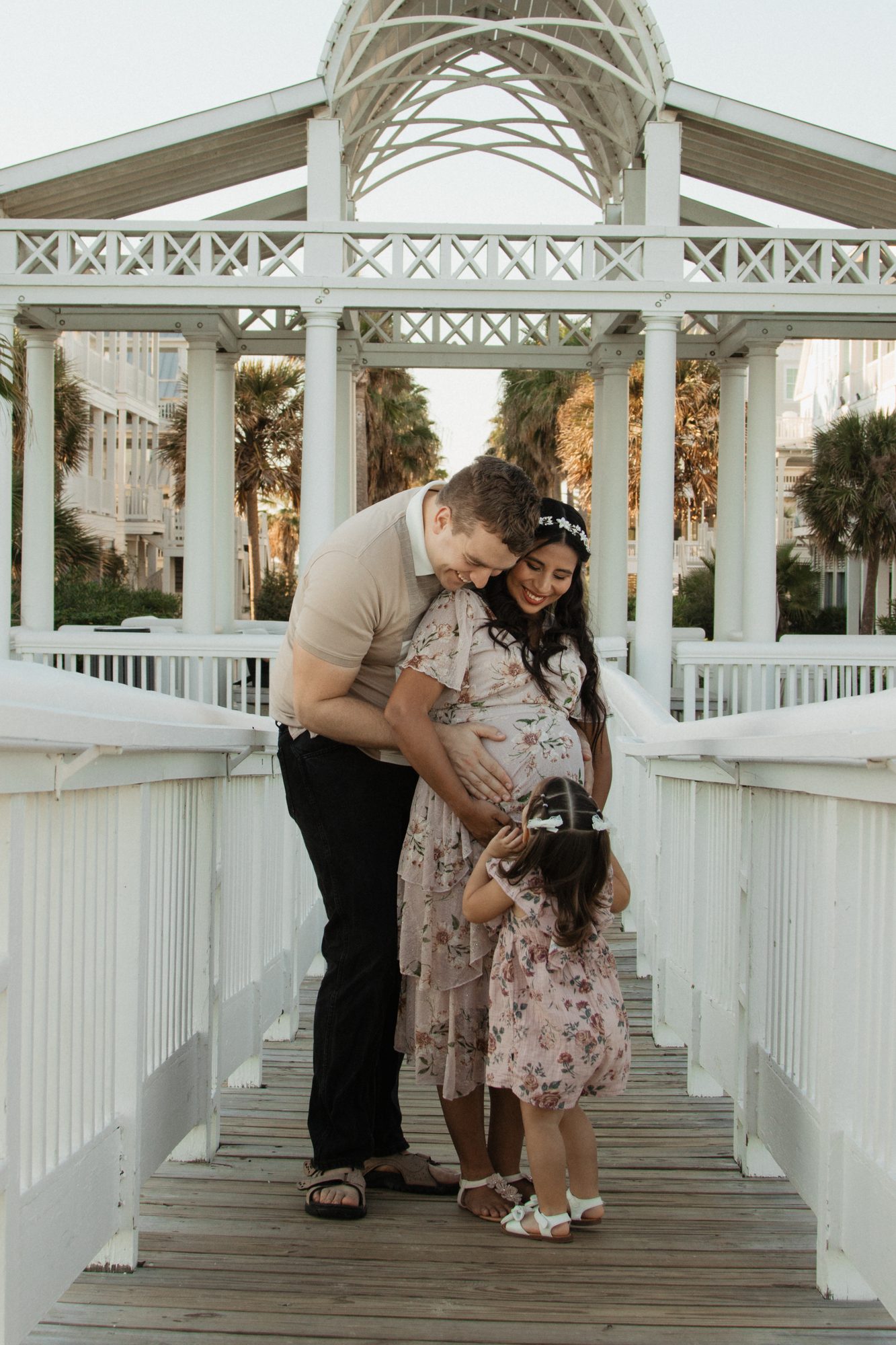 Family of three embracing under a white gazebo during a maternity session