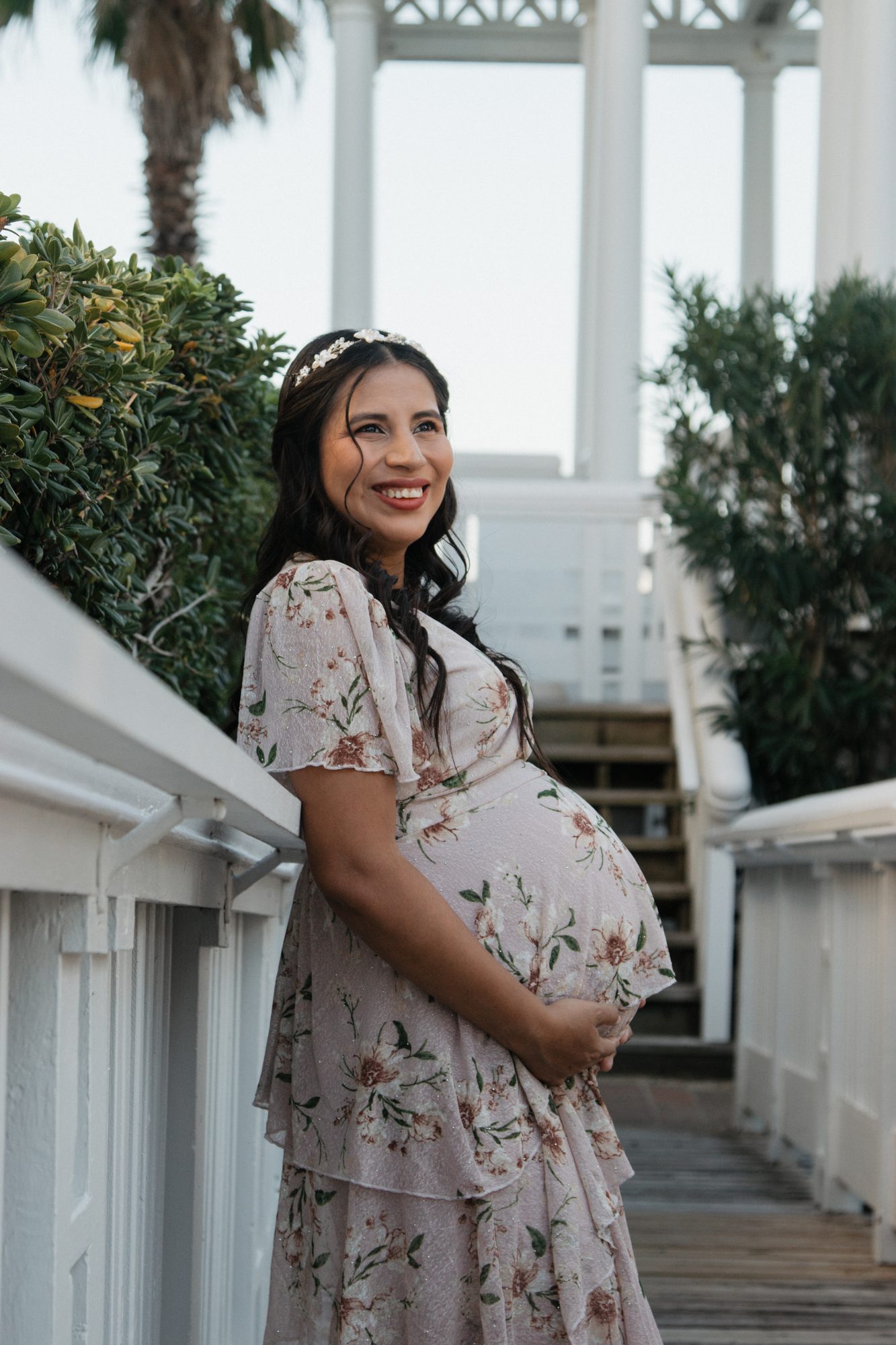 Expecting mom smiling and holding her bump on a white boardwalk in Galveston