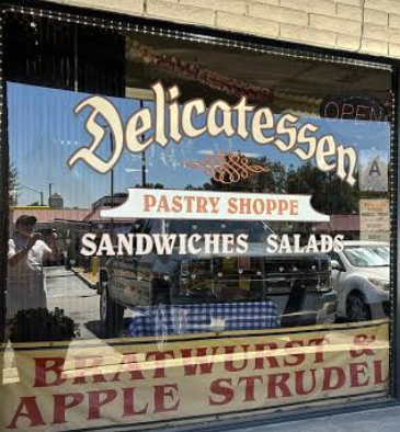 Front window sign of Upland German Delicatessen on Route 66 showing gold and cream lettering for Delicatessen, Pastry Shoppe, Sandwiches, Salads, Bratwurst and Apple Strudel