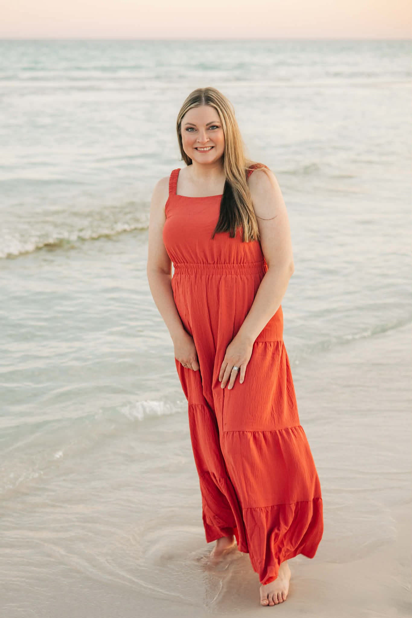 Amber Renee Till in a red dress on the beach walking in calm water