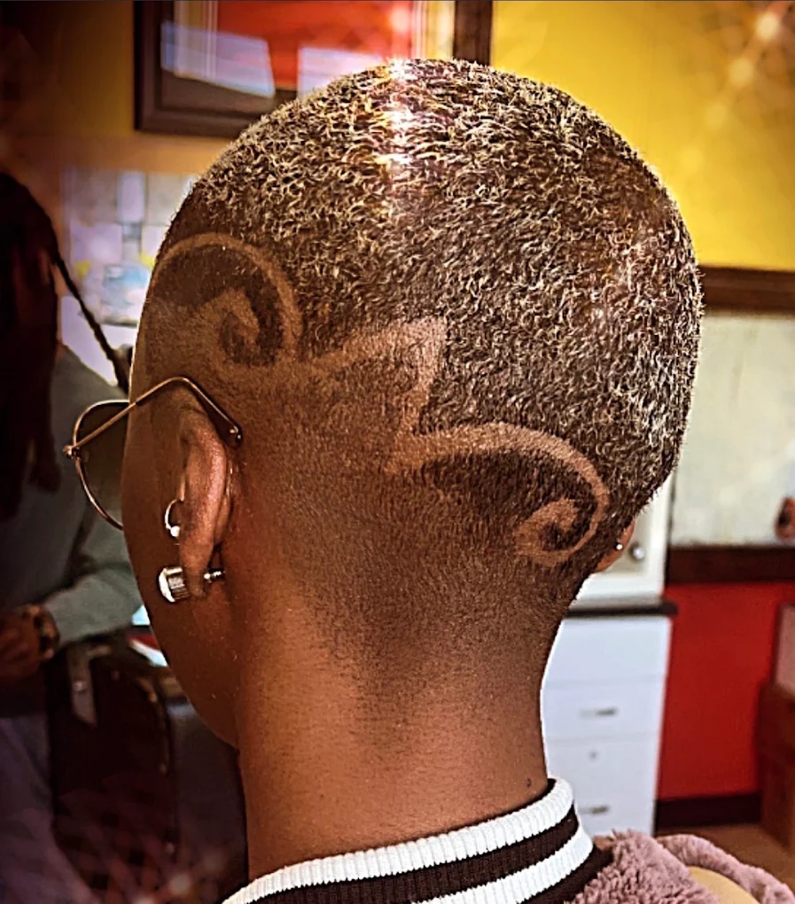 Platinum blonde buzz cut featuring intricate dual wave swirl razor art and sharp nape taper