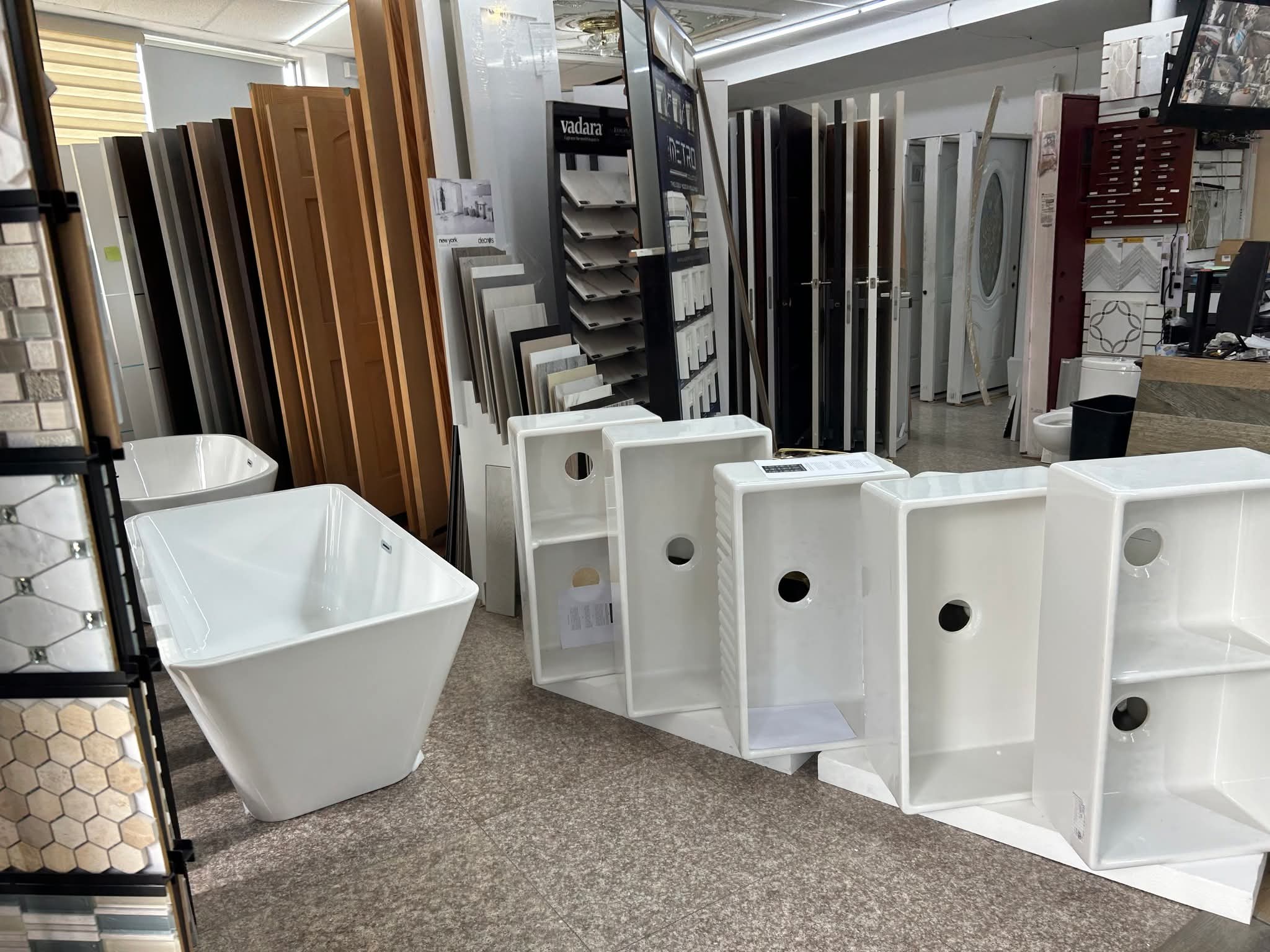 Showroom floor with white apron sinks, soaking tub, tile sample boards, and door displays
