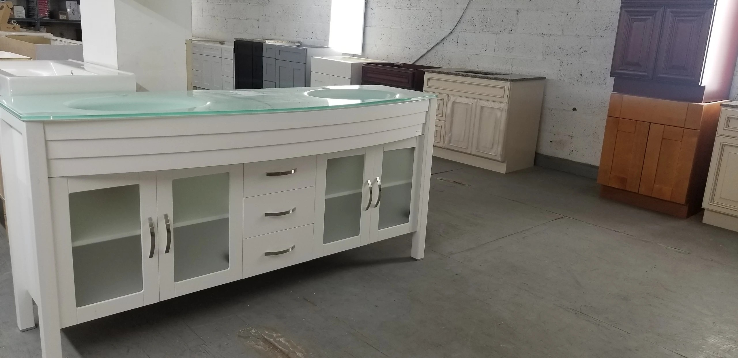 Modern white double vanity with glass top and frosted doors on warehouse floor