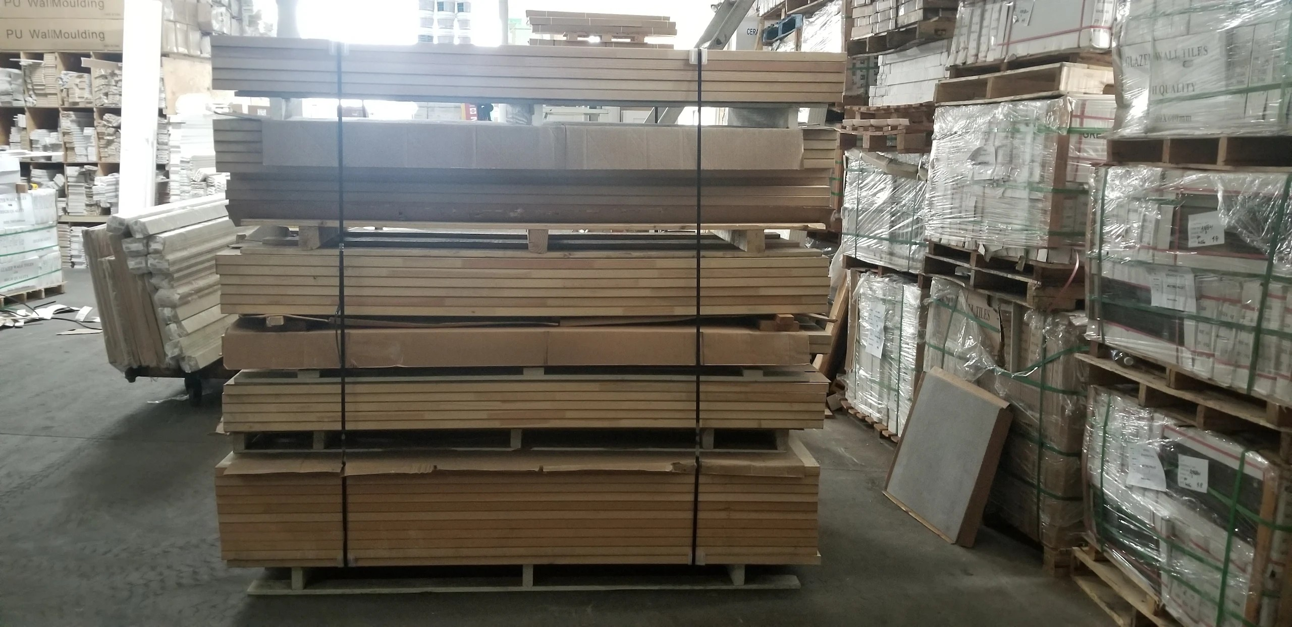Strapped pallets of moulding, trim, and glazed wall tiles in warehouse