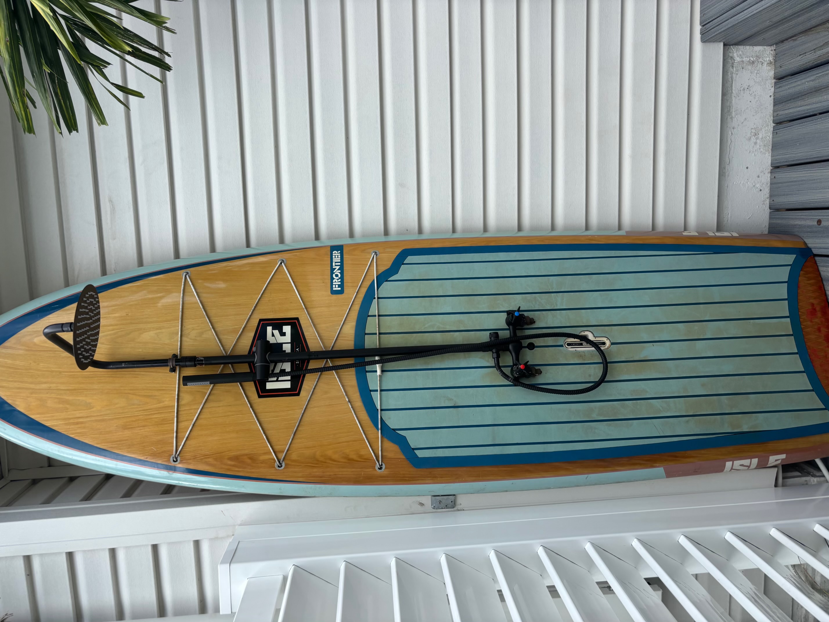 Detailed view of matte black outdoor shower plumbing and rainfall head mounted on a wood-tone surfboard