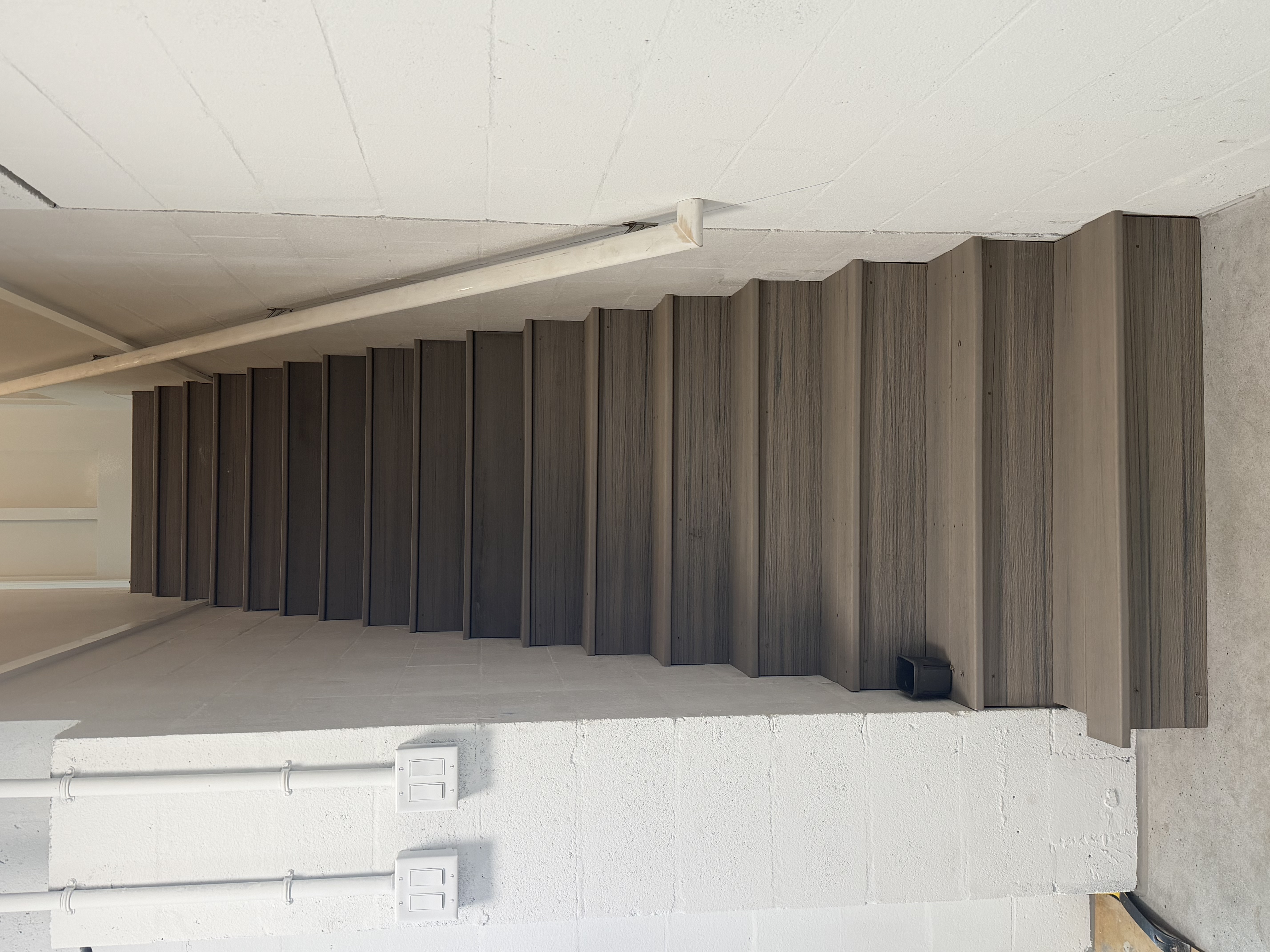 Full completed interior staircase with dark wood-grain composite treads, risers, and handrail against white block wall