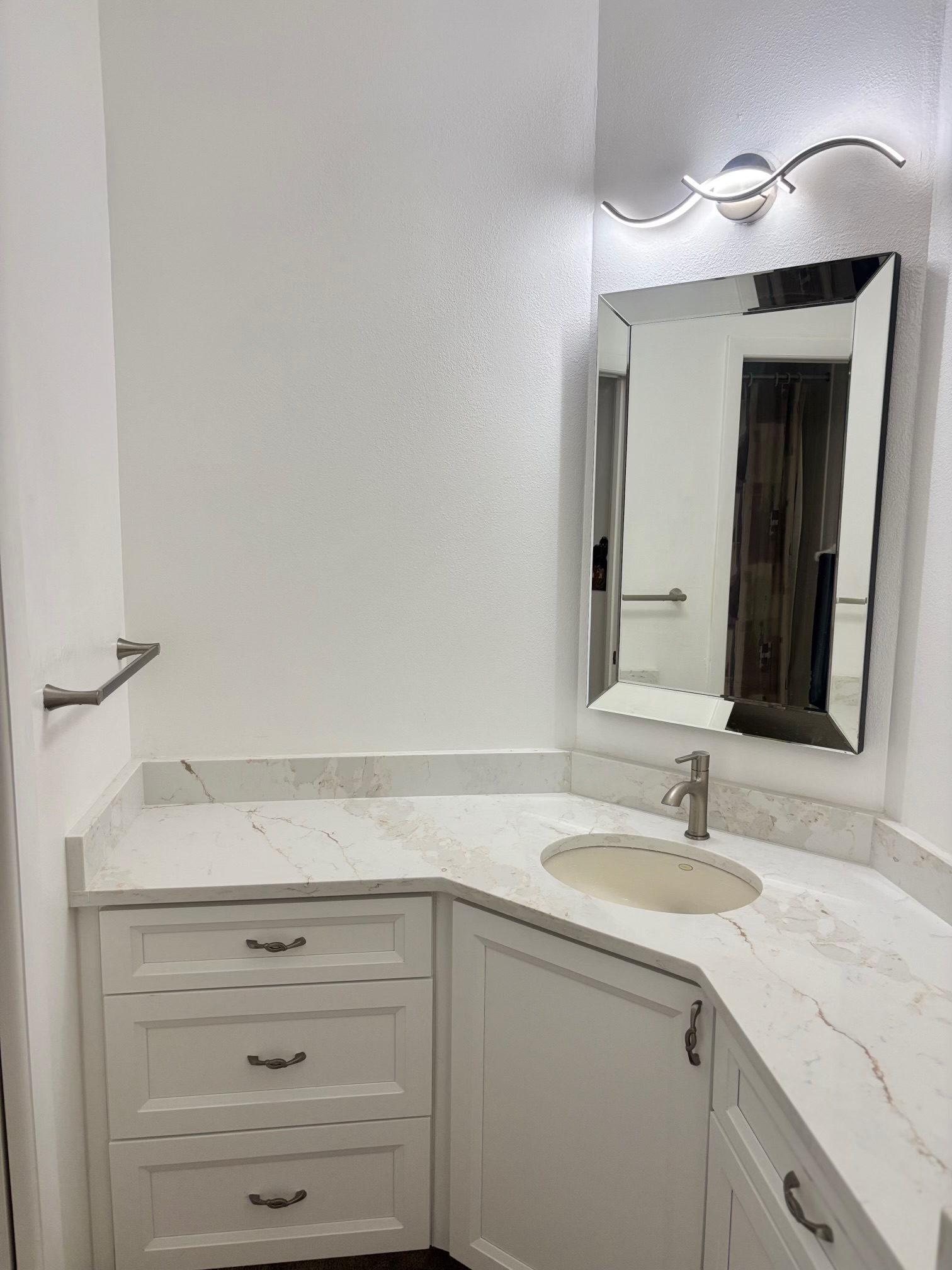 Vertical view of bathroom vanity with modern curved LED light fixture, large beveled mirror, and quartz countertop