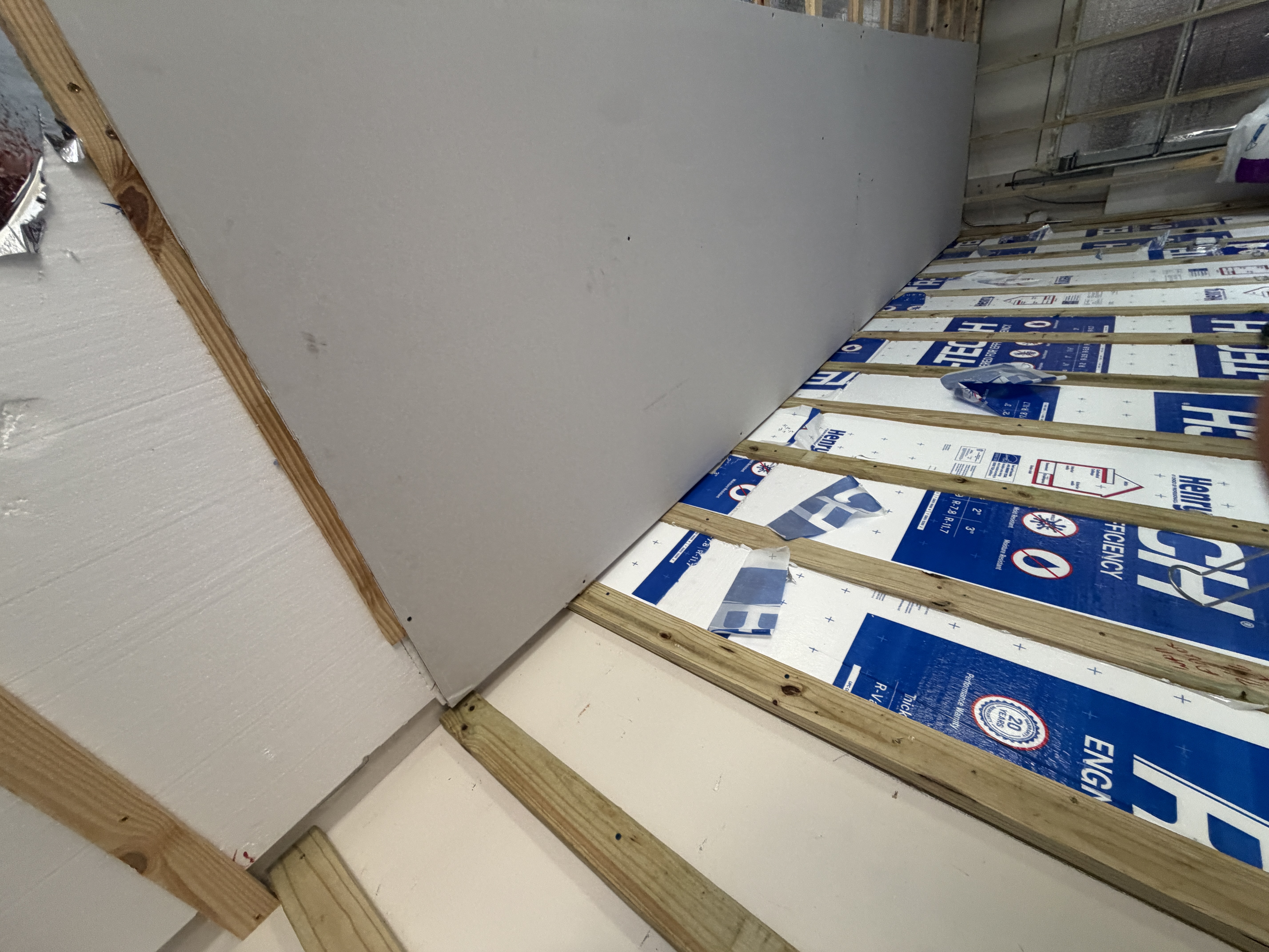 Furring strips, foam insulation board, and new drywall sheet installed along an interior masonry wall