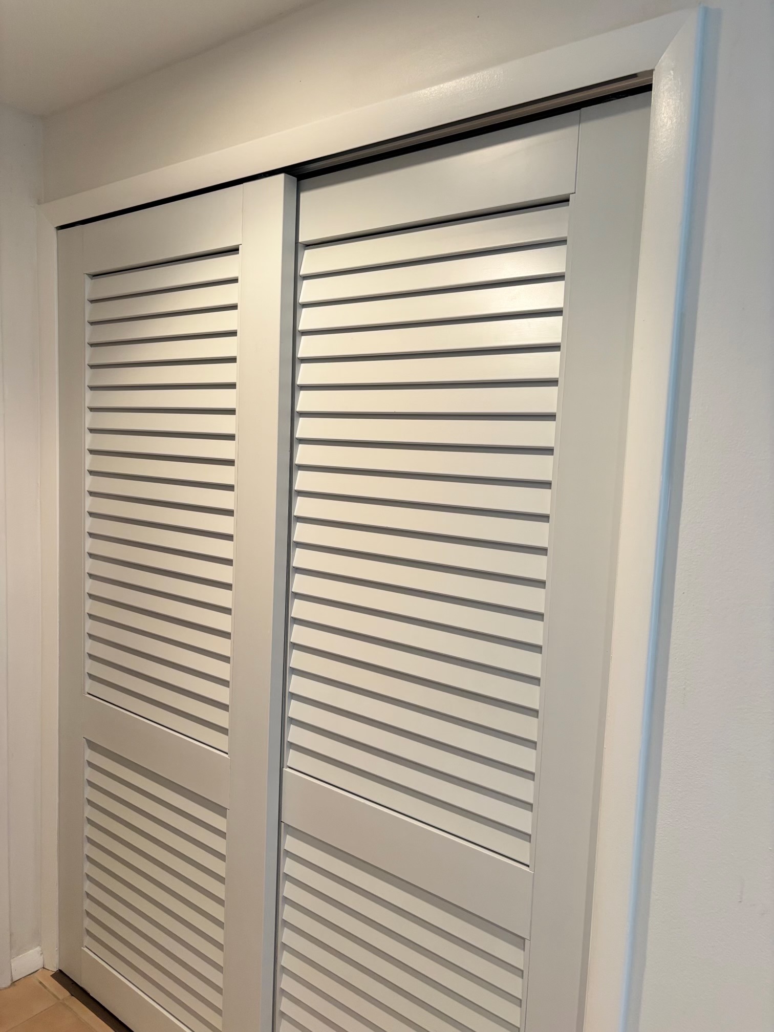 Custom white louvered bifold interior closet doors with white trim casing and smooth track hardware