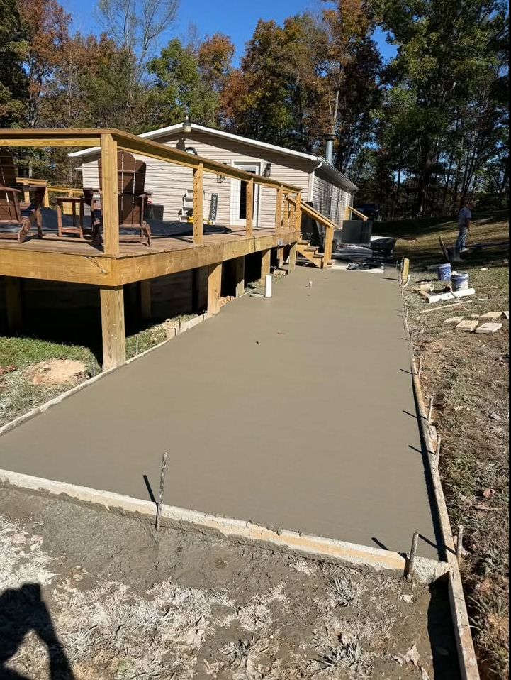 Freshly poured smooth concrete walkway beside deck after completion