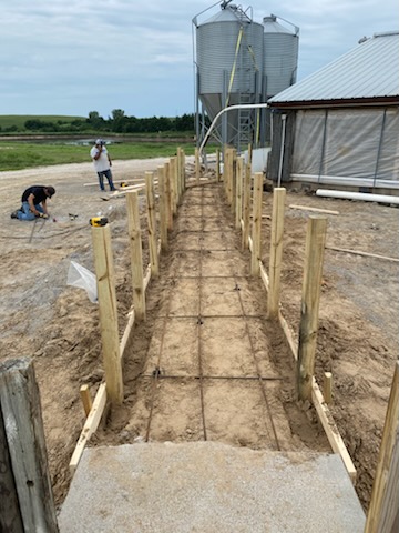 Agricultural pathway framing, rebar grid, and wood posts near silos